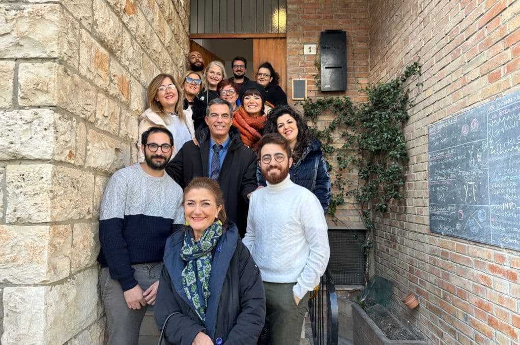 Group of people gathered at the entrance of Casa Netural Matera, showing the stone facade and front door with the number 1 (Via Galileo Galilei 1)