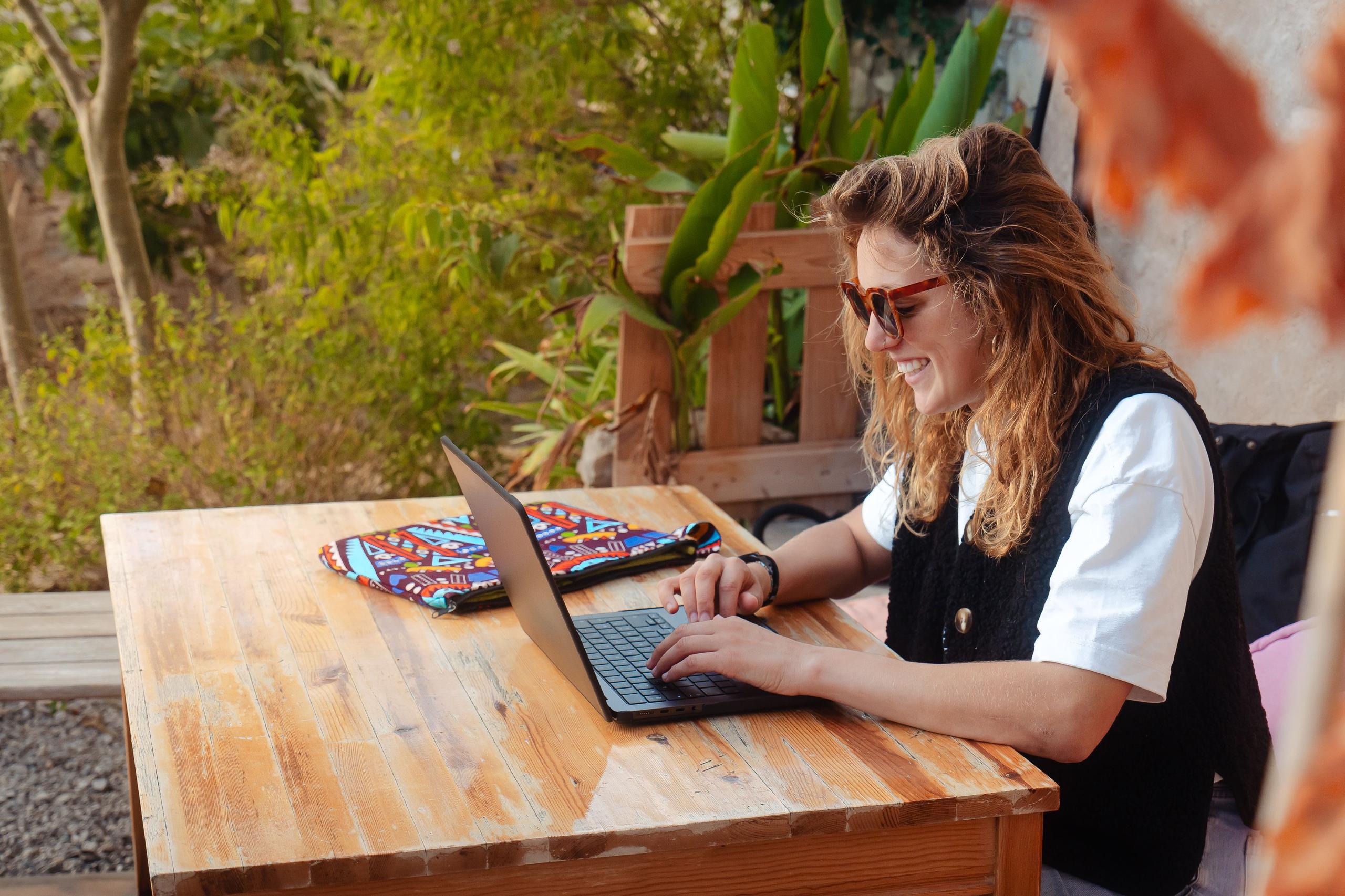 A woman working on a laptop at the shaded outdoor table in the garden
