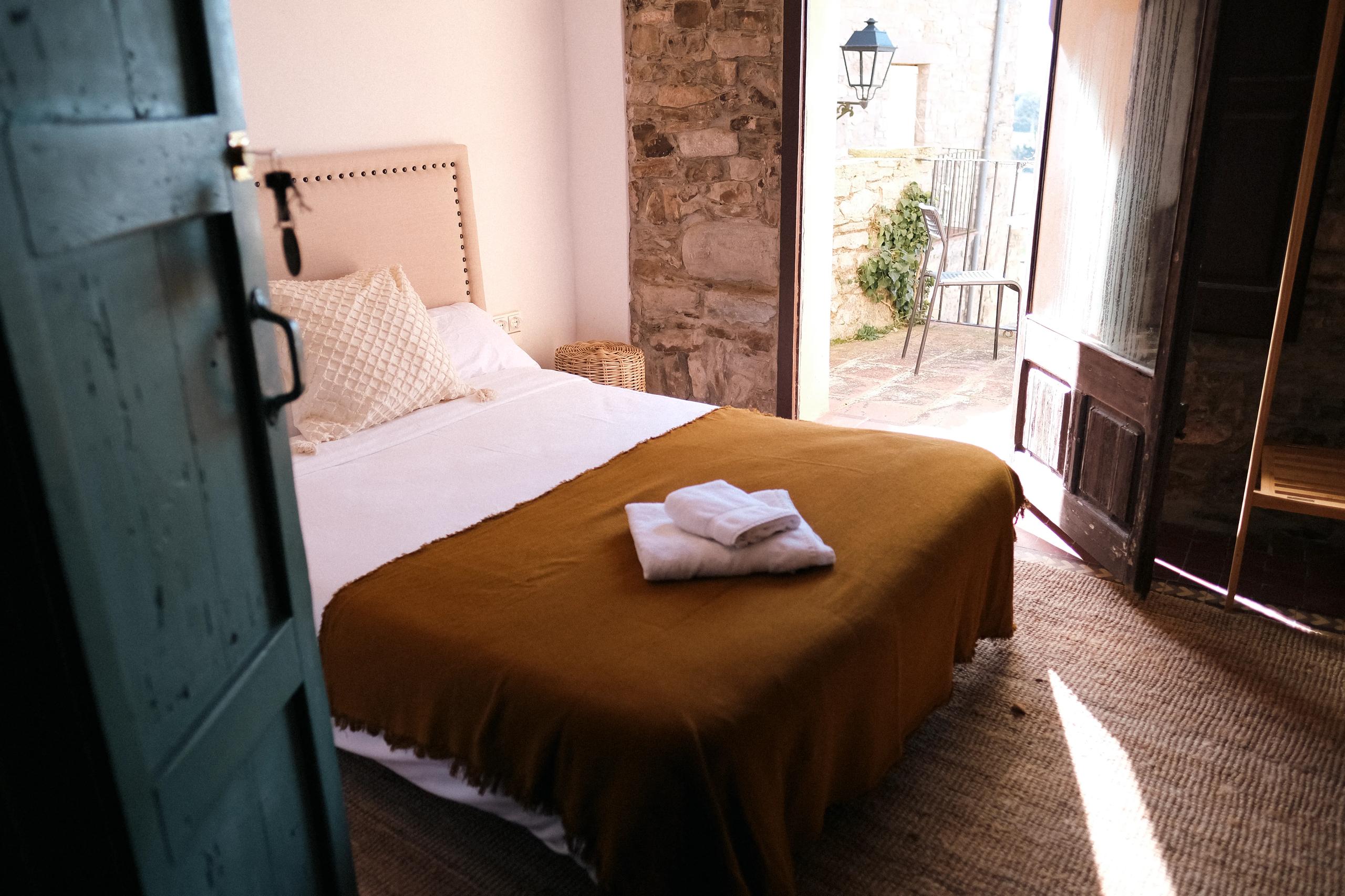 A private double room with access to a terrace, featuring a mustard-colored blanket and stone wall