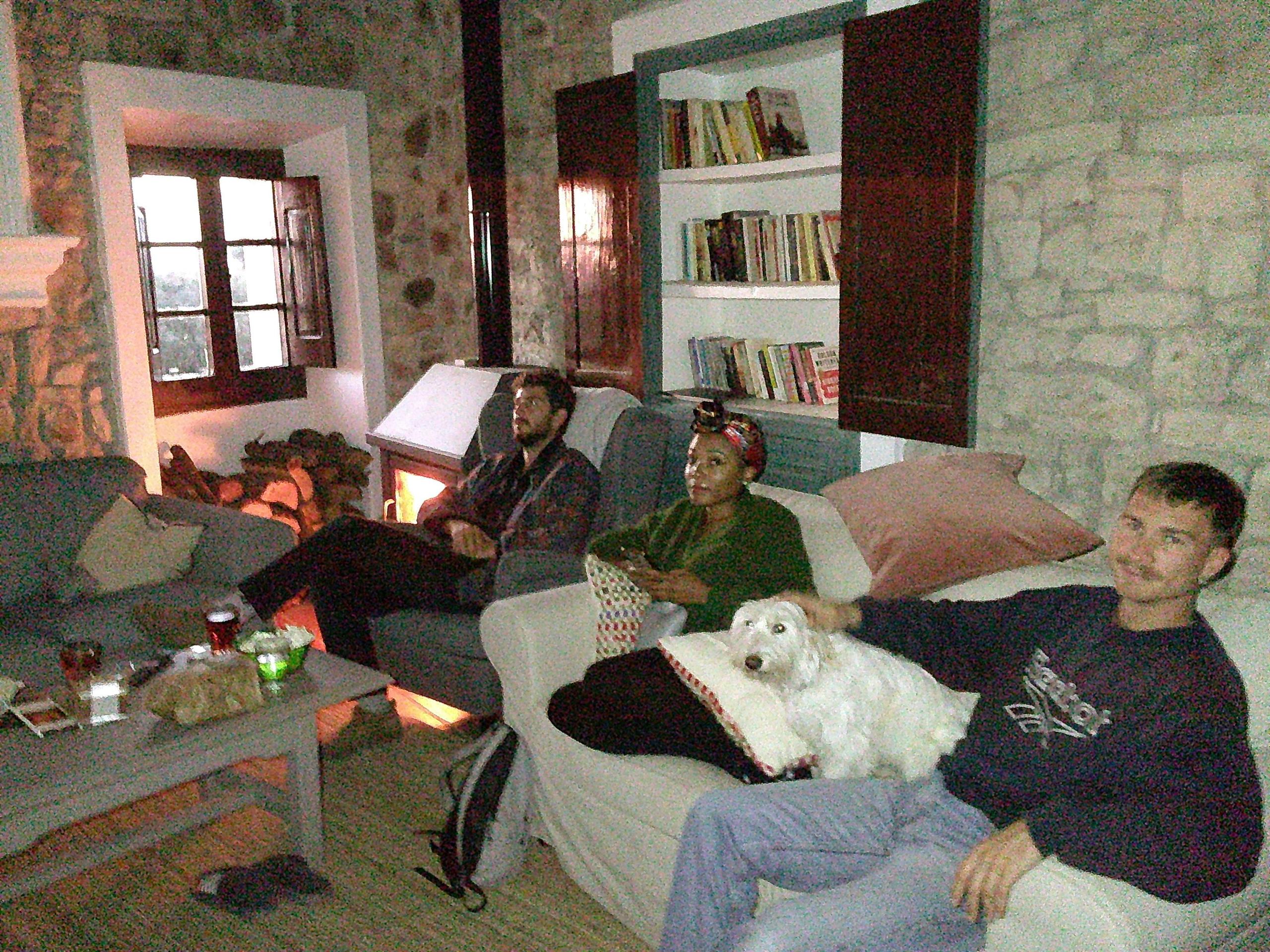 Casa Pardal coliving guests relaxing in the stone-walled living room, watching a movie together by the fireplace during a cozy evening