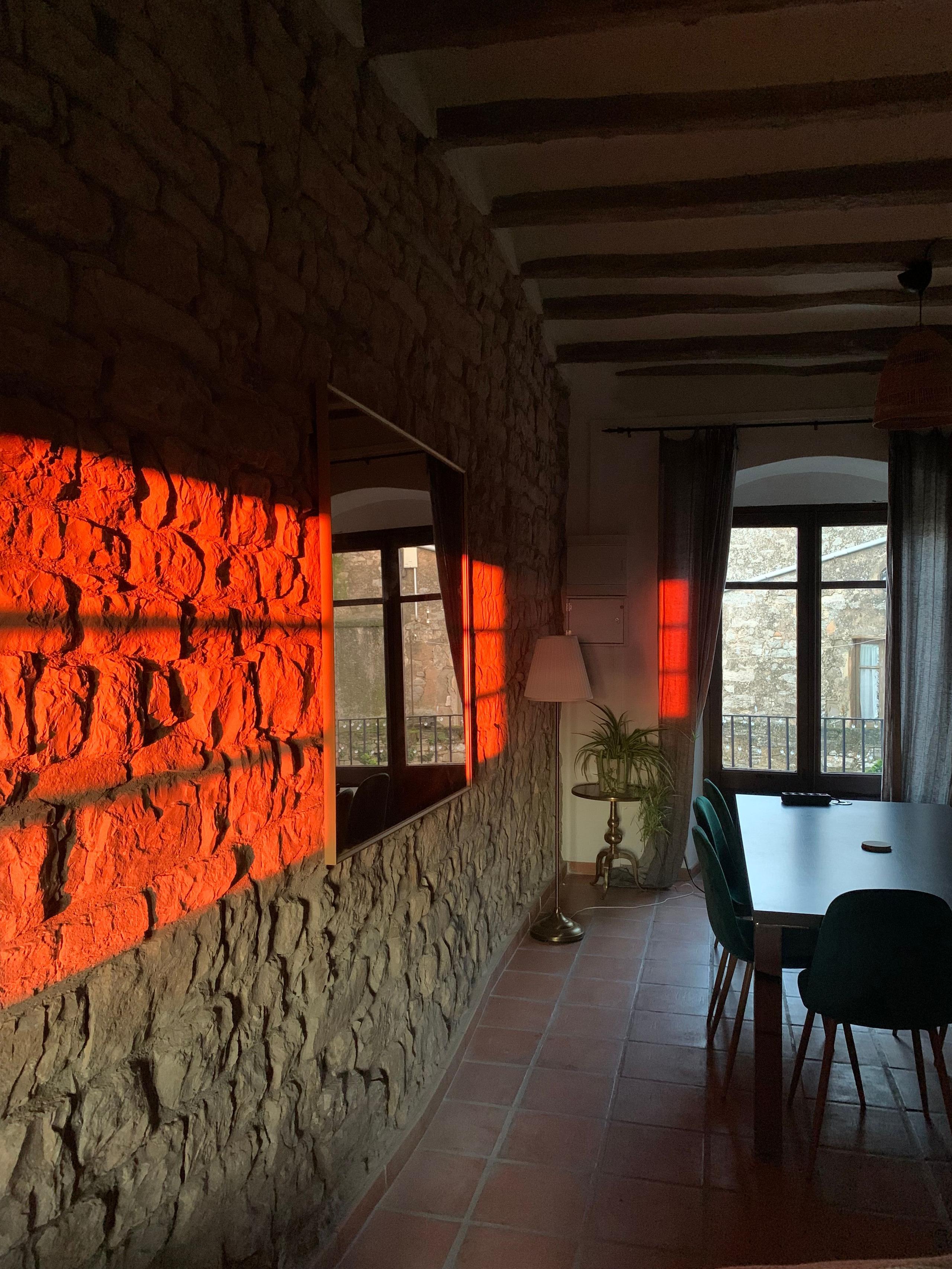 Golden-hour sunlight reflecting off the stone wall inside Casa Pardal's dining and coworking room with rustic beams and large windows