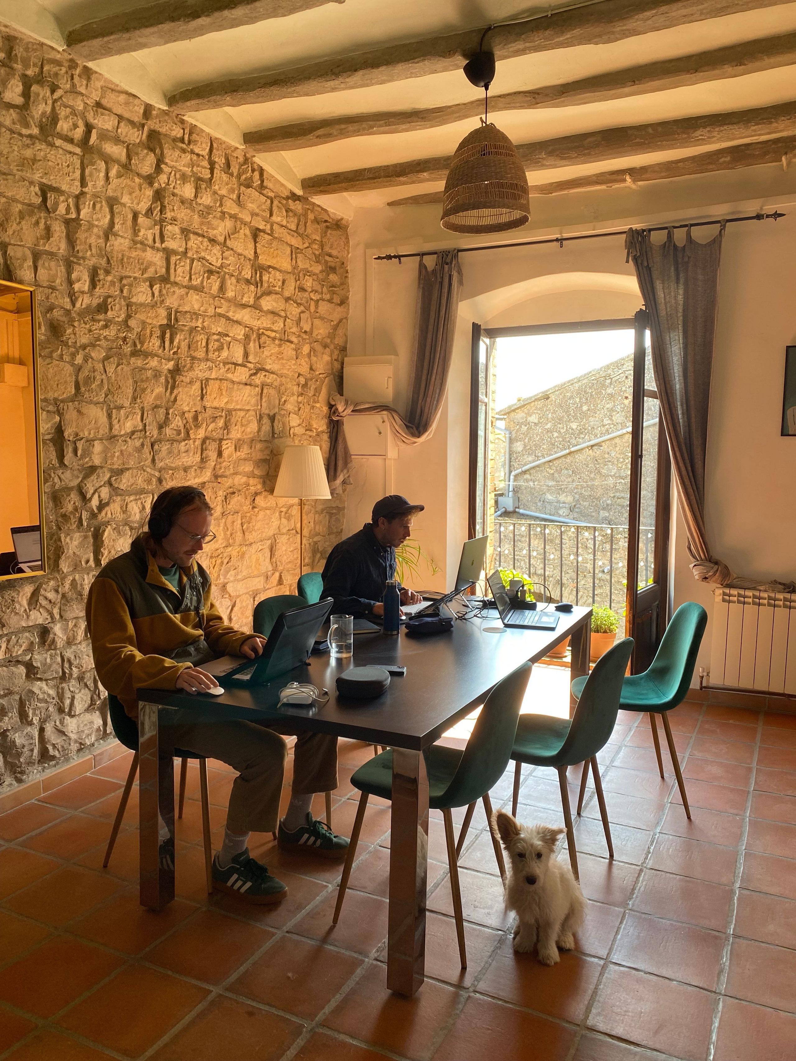 Two people working on laptops at the coworking table in the stone-walled coworking room