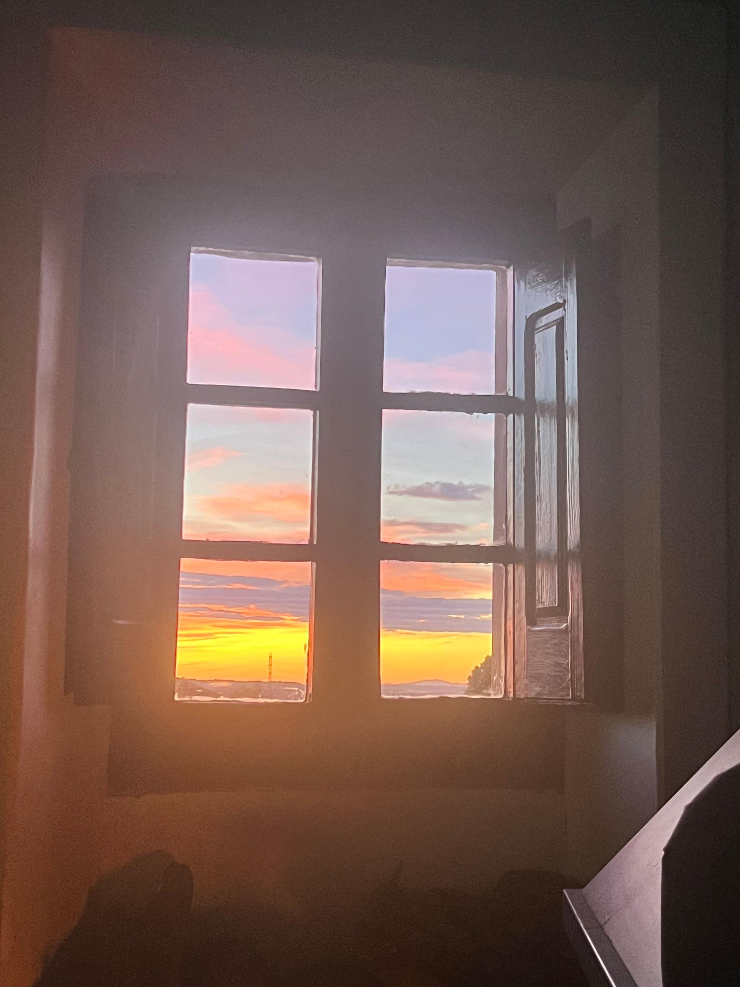 Sunset view through a rustic wooden window at Casa Pardal in Catalonia, with pastel skies and golden light filling the room