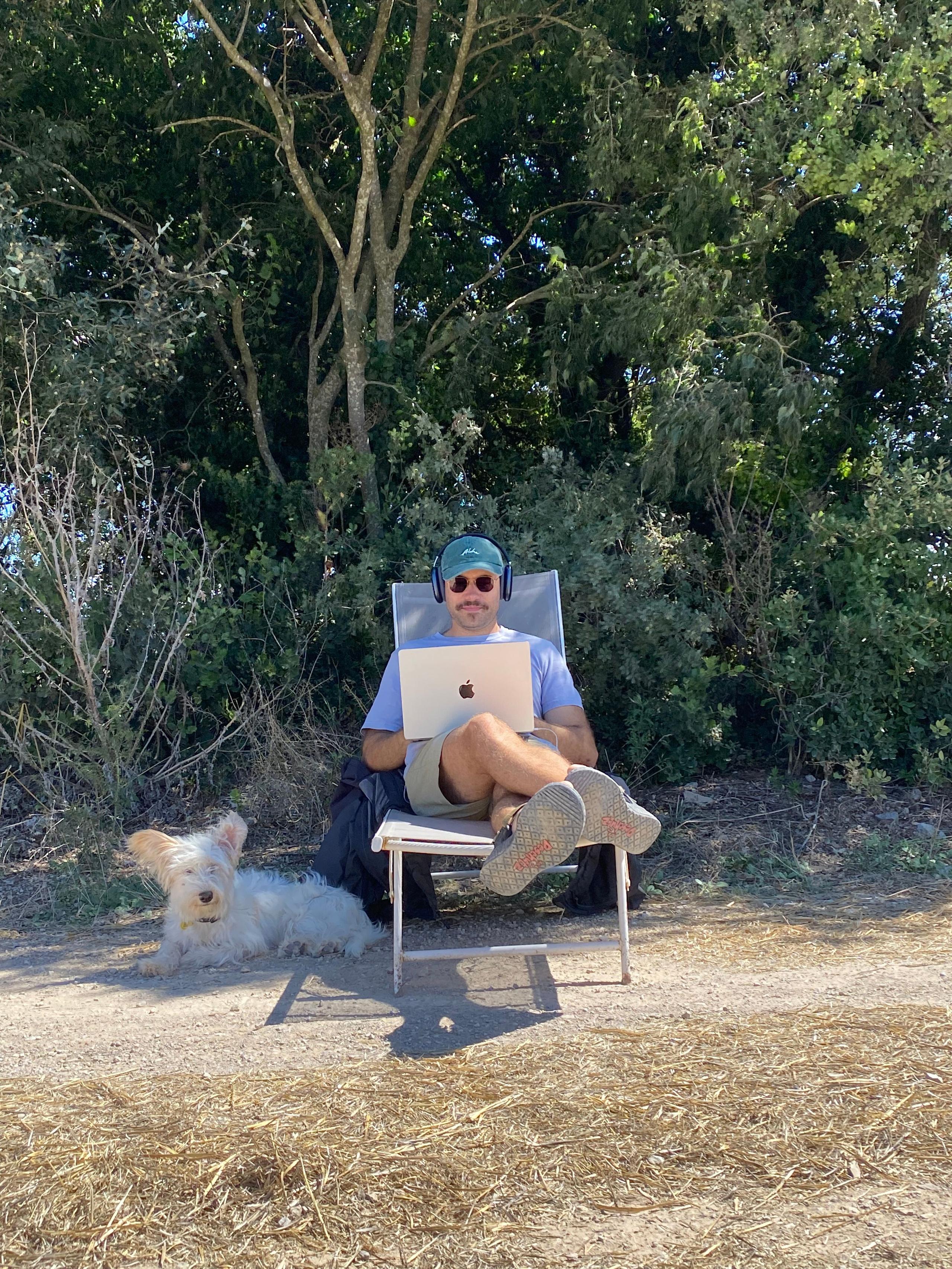 A man working on a laptop outdoors in a chair surrounded by trees