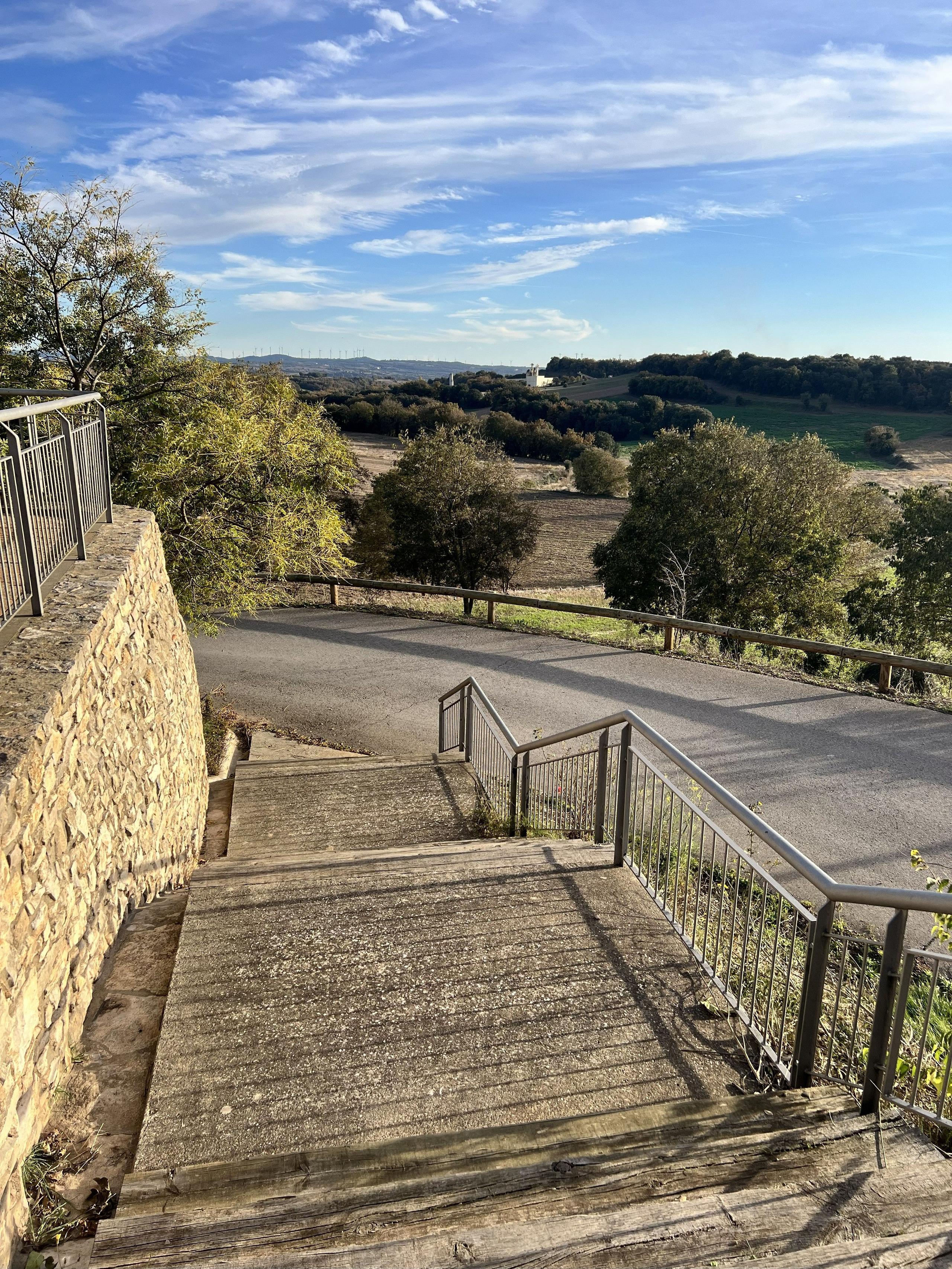 Wooden steps at Casa Pardal overlooking the rural Catalonia landscape, with open fields, trees, and hills under a bright blue sky