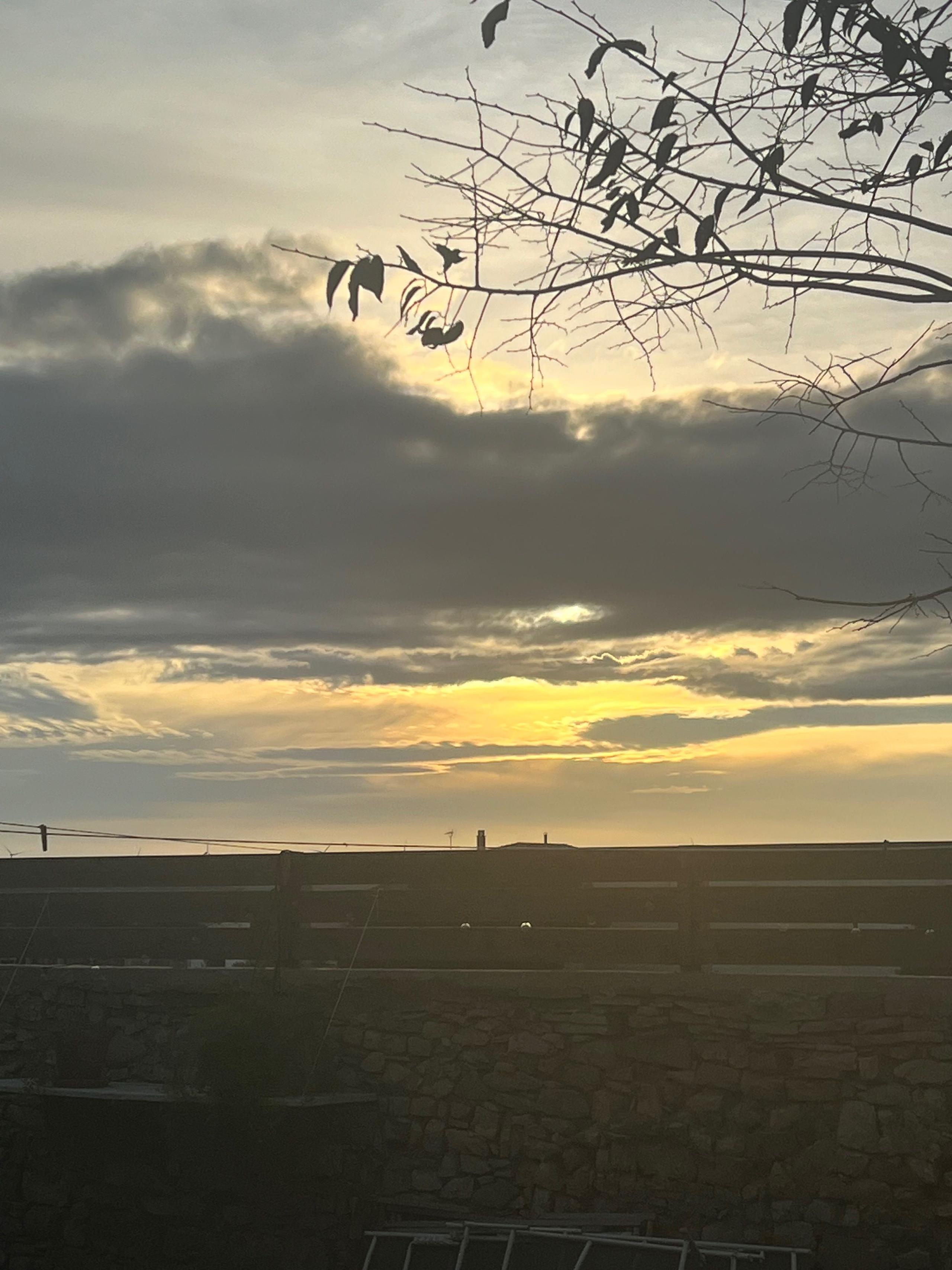 Sunset view from Casa Pardal with golden light breaking through clouds and silhouetted tree branches