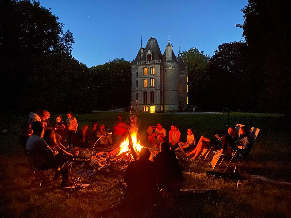 Colivers gathered around a bonfire in front of the illuminated château at night
