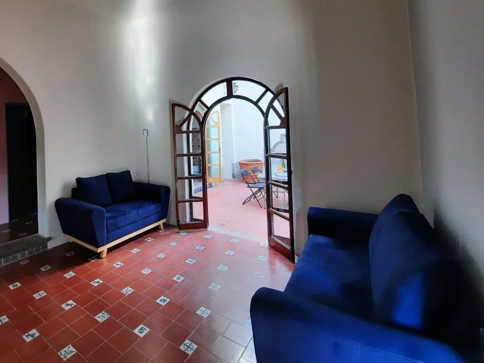 Living room with two blue sofas and an arched wooden door opening to the terrace