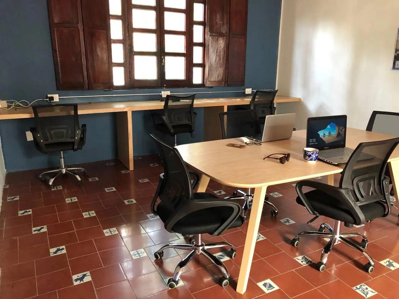 Coworking area with a long wall-mounted desk, central table, multiple mesh office chairs and a laptop