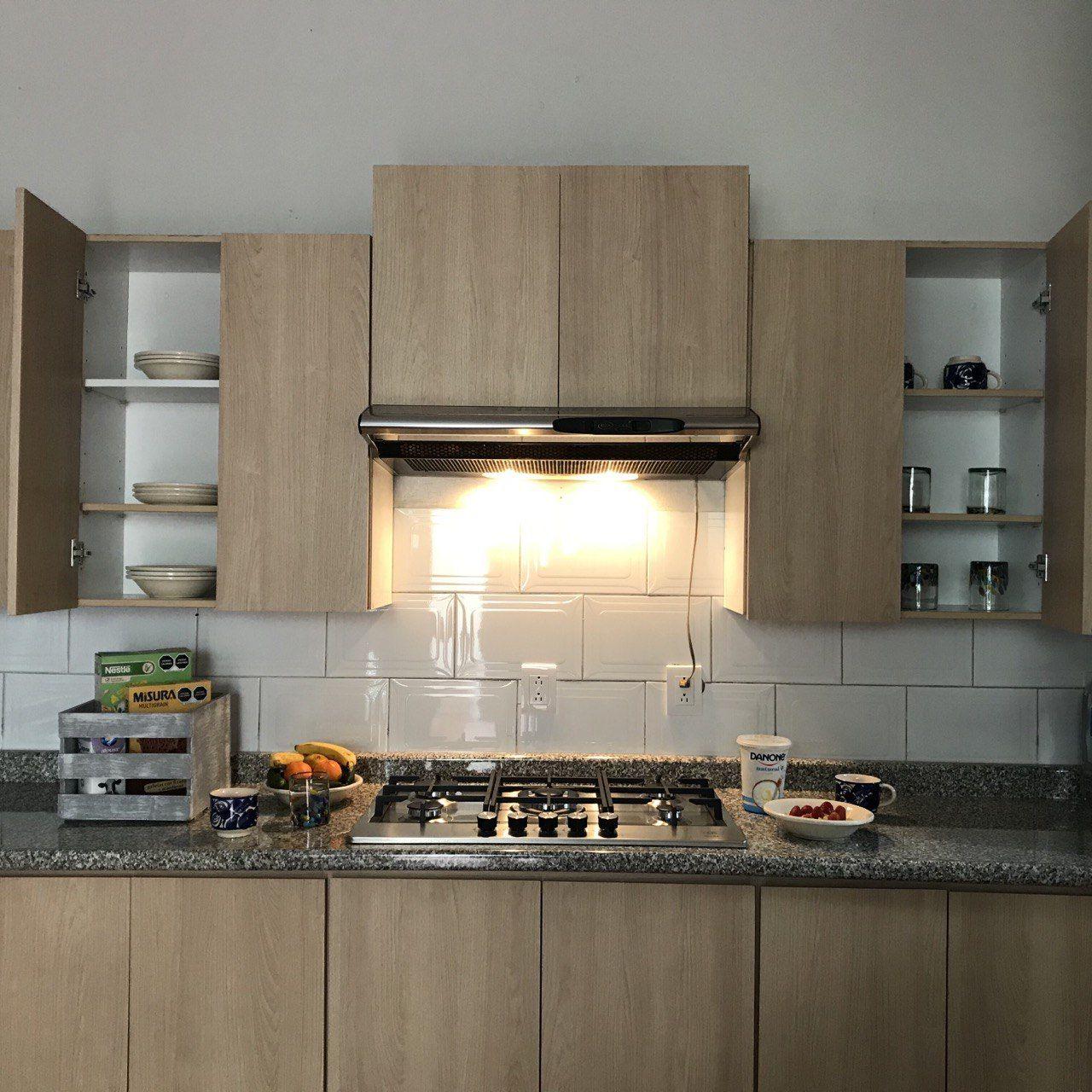 Shared kitchen with light wood cabinets, gas stove, range hood and food items on the counter