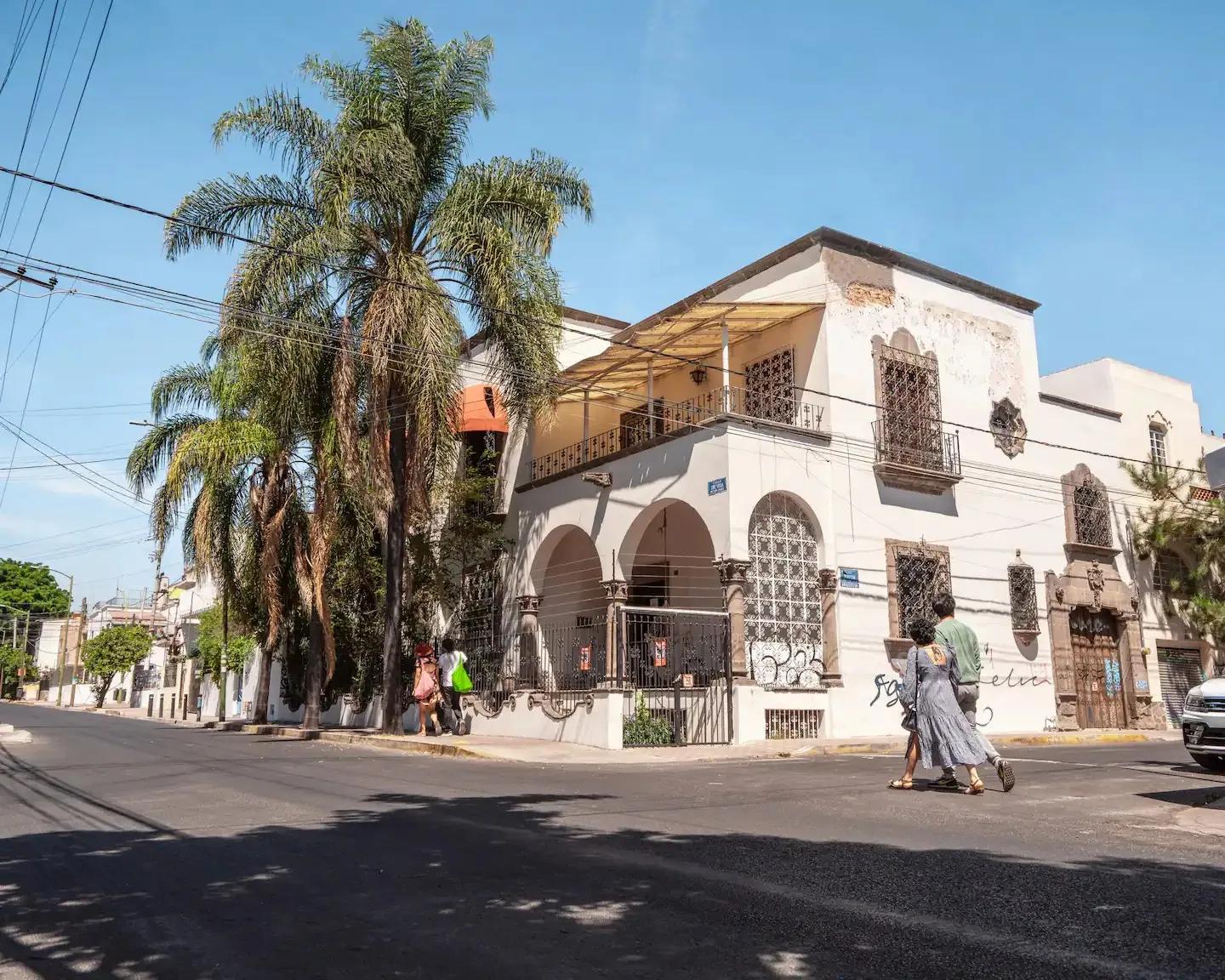 White colonial-style building at street corner with palm trees, arched facade and iron gate