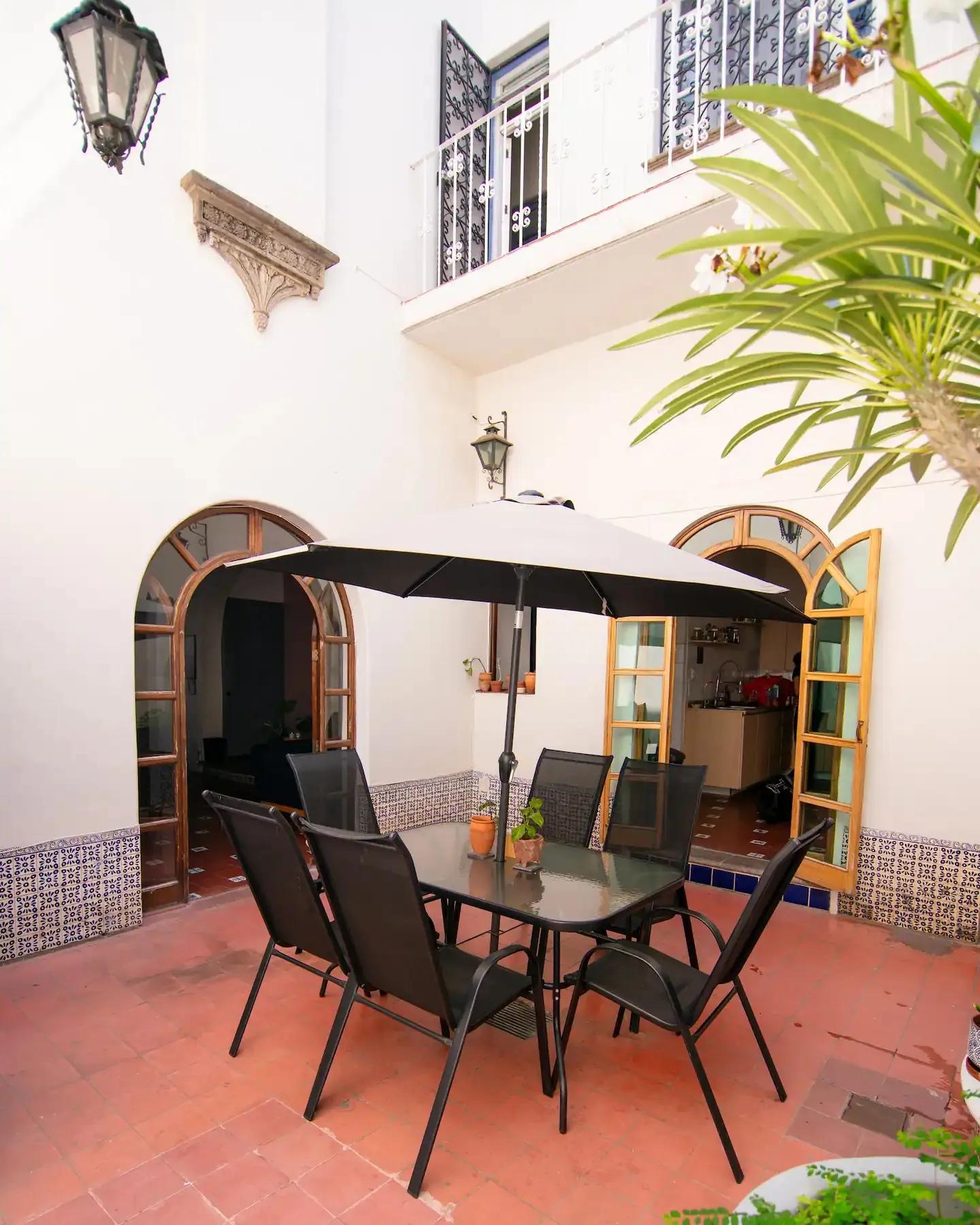 Open-air courtyard with a dining table and chairs under a black umbrella, arched doorways and balcony above