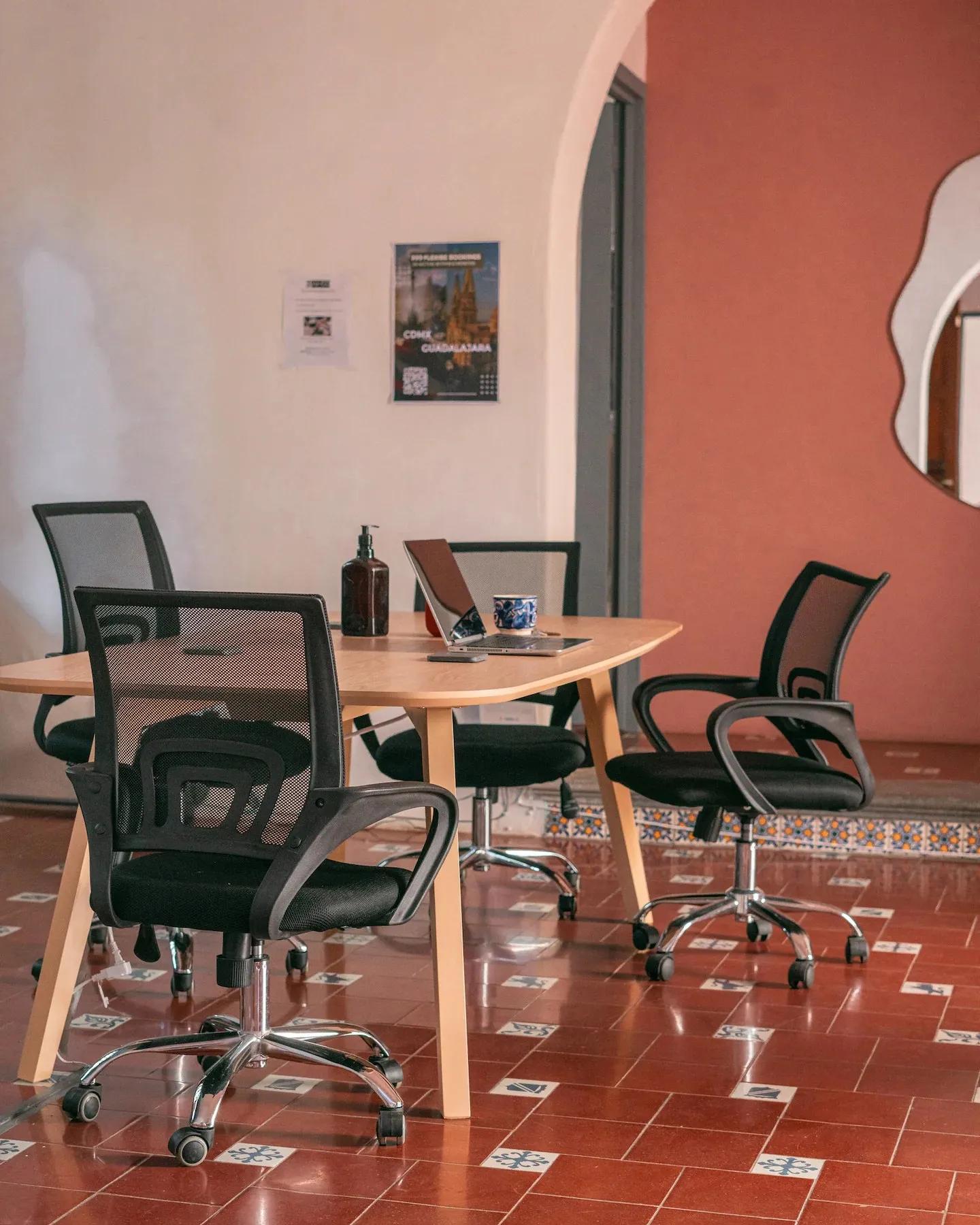 Coworking area with a large wooden table, mesh office chairs, laptop and a Guadalajara poster on the wall