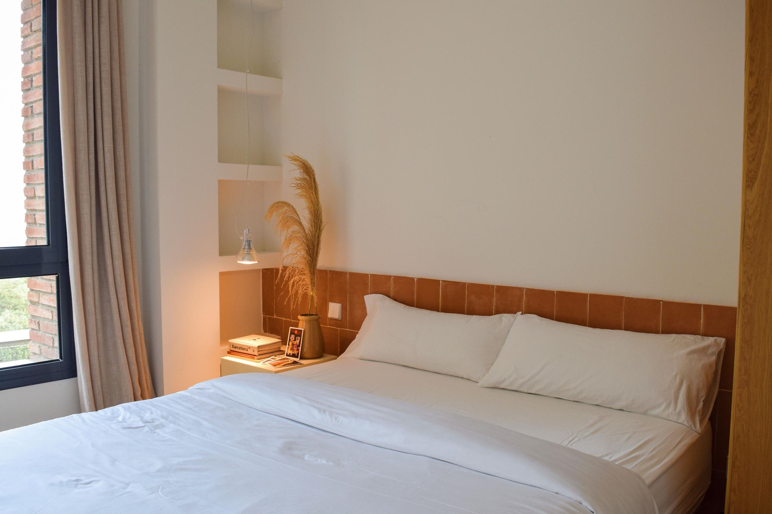Queen room with white bedding, terracotta tile headboard, and a window with natural light.