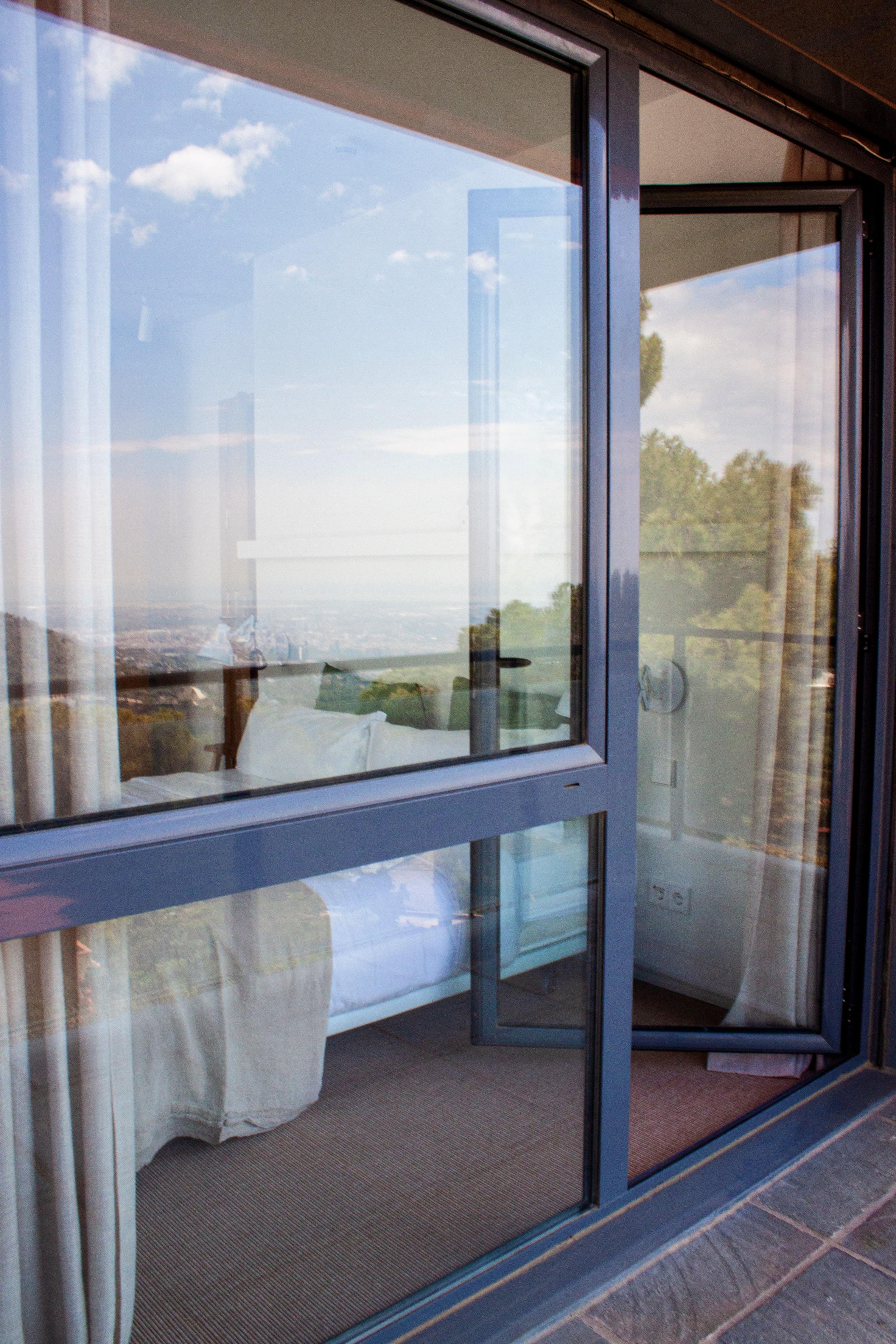 View through the glass terrace door of a king studio, showing the bed inside and the city/sea view beyond.