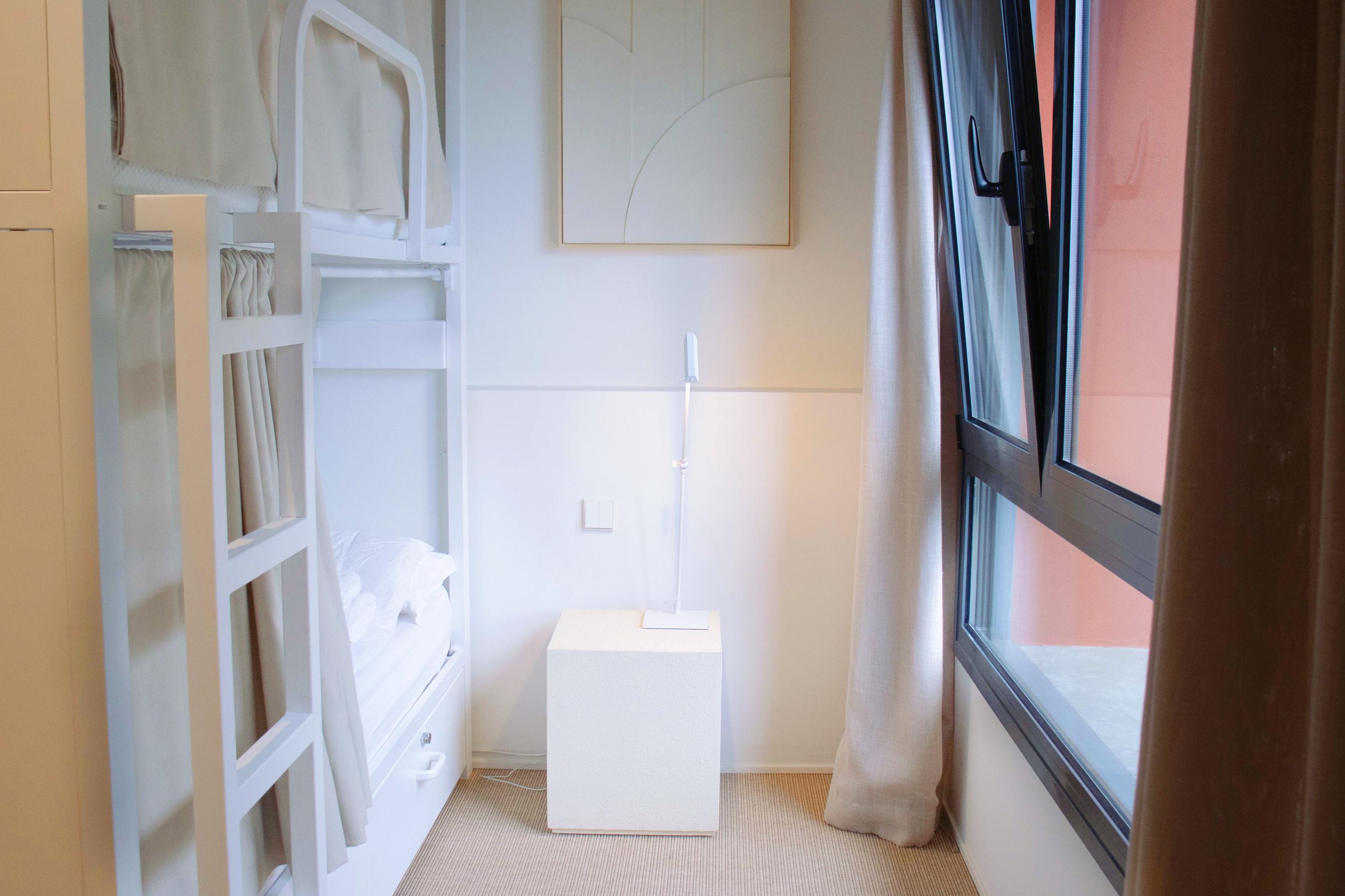 Shared suite with white bunk beds, curtains for privacy, and a window with natural light.