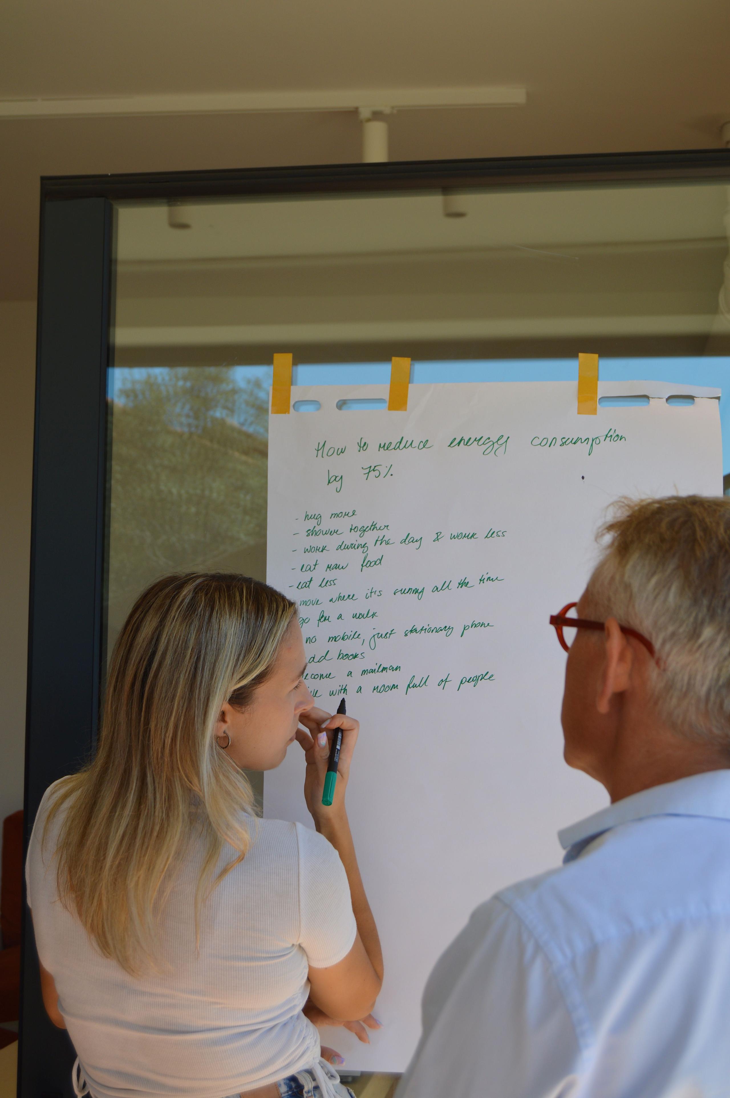 Two people at a workshop, writing on a flip chart about reducing energy consumption.