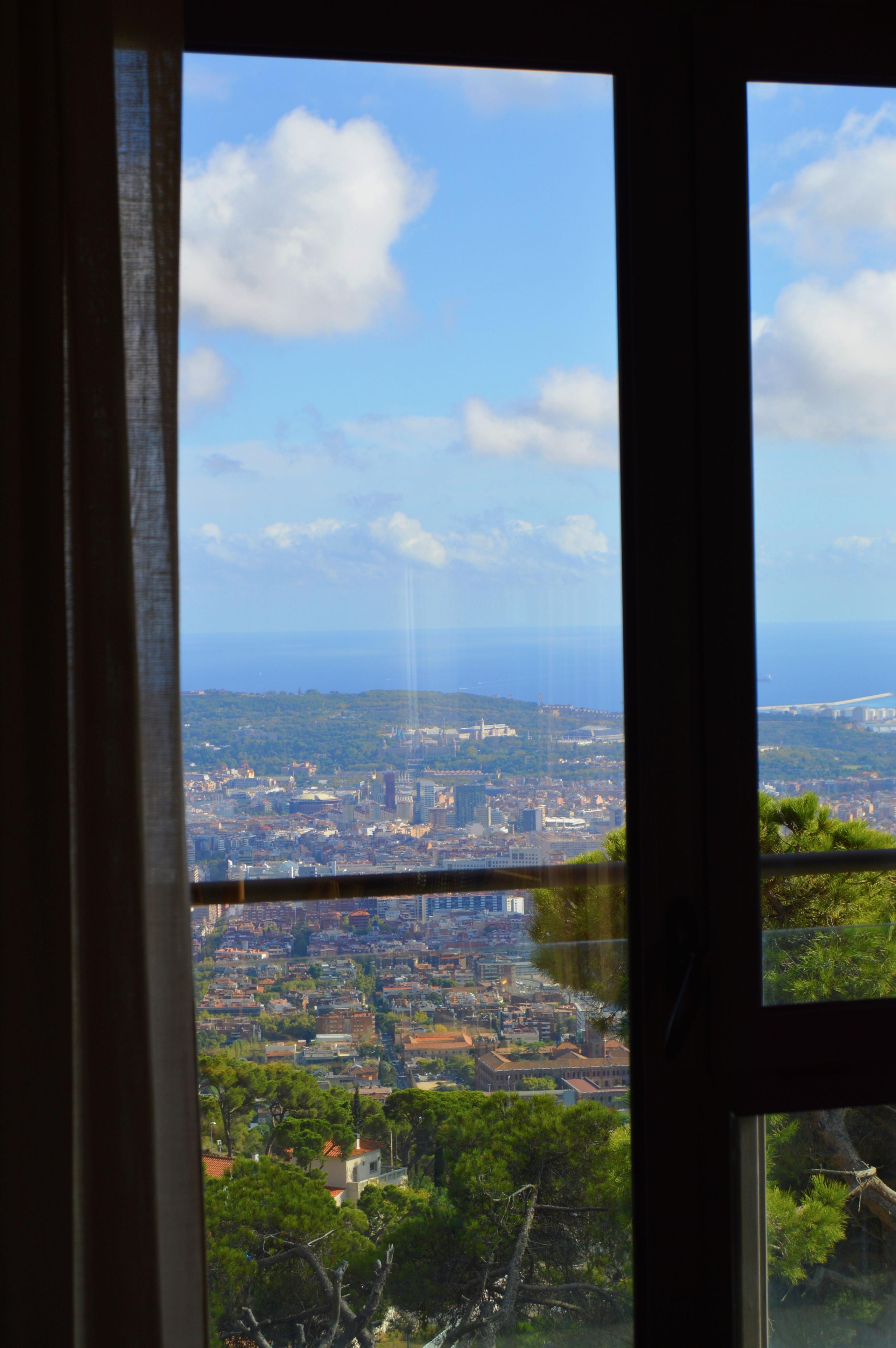 View of Barcelona city and the sea through a room window, with curtains framing the panoramic vista.