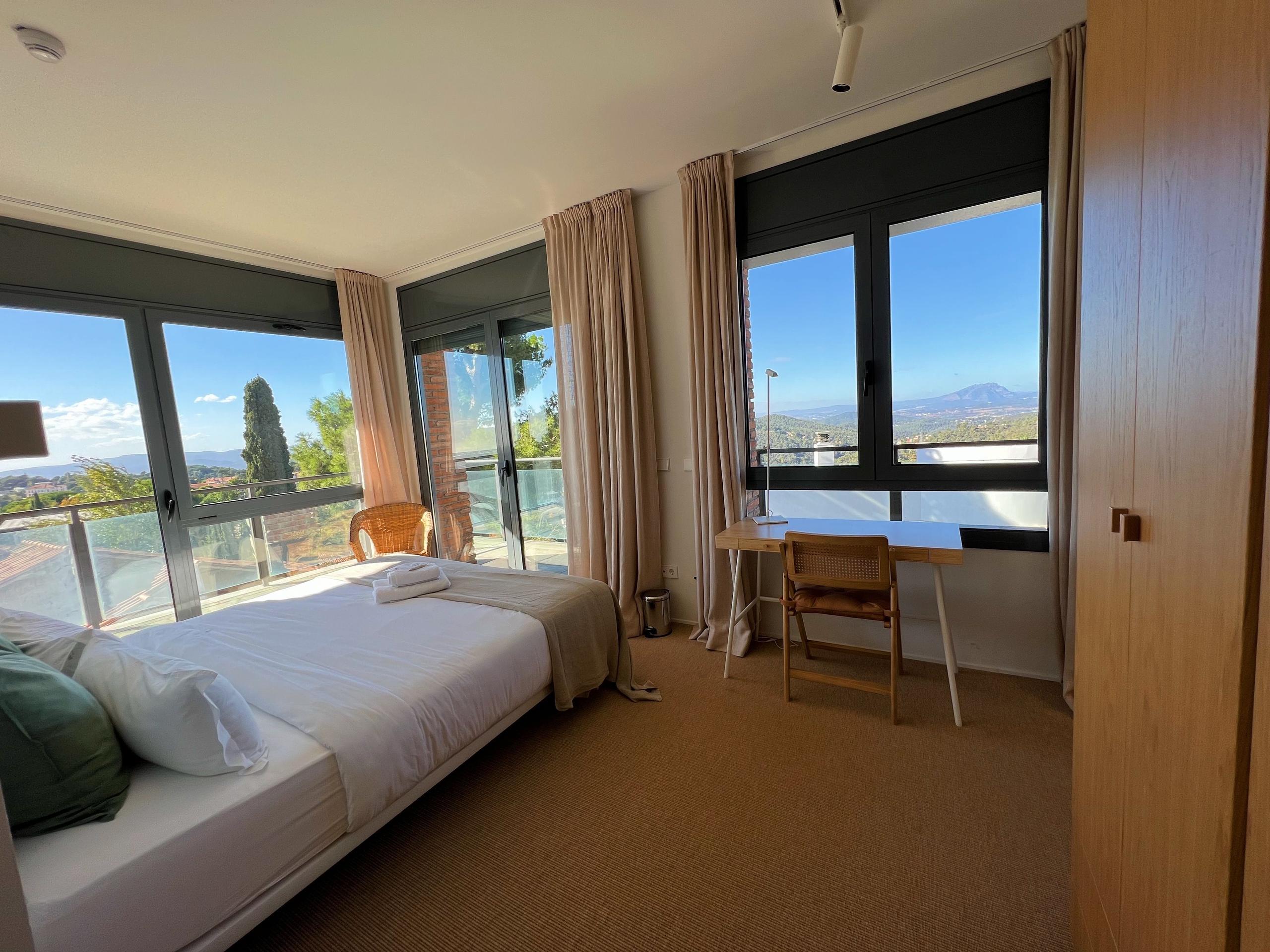 Bright king studio room with large panoramic windows, a king bed, desk, and private terrace with mountain and sea views.