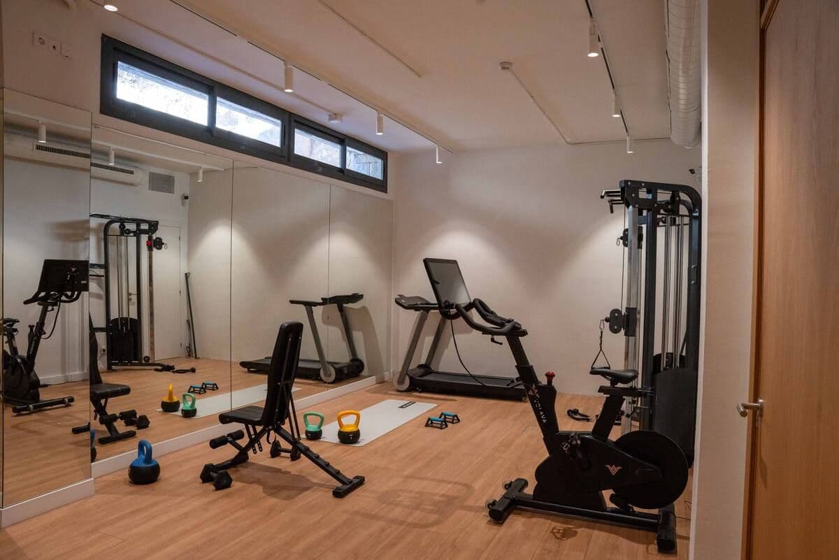 On-site gym with a treadmill, stationary bike, cable machine, weight bench, kettlebells, and large mirrors.