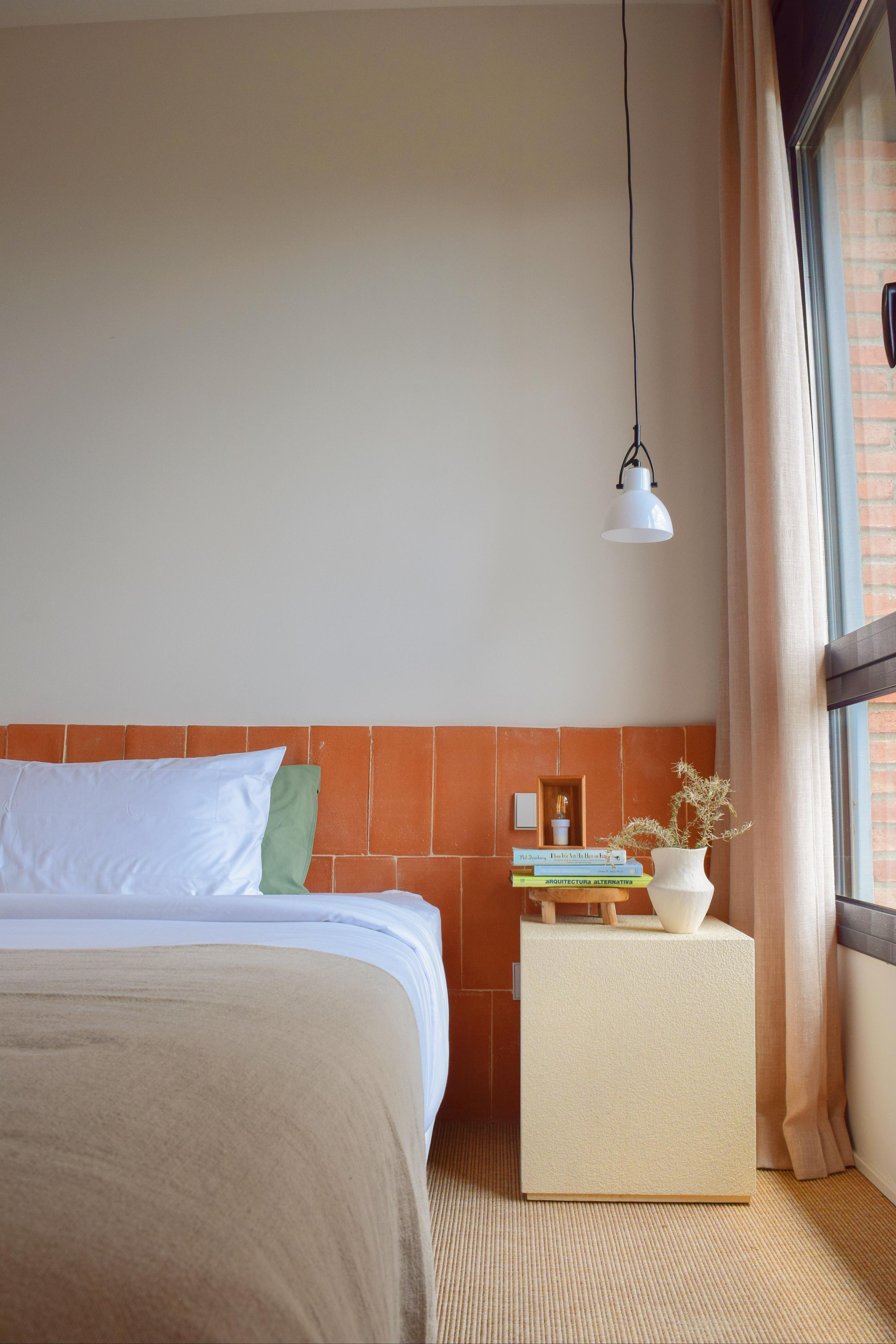 Queen suite bedroom with terracotta tile headboard, white bedding, a pendant lamp, and a vase with dried flowers on the nightstand.