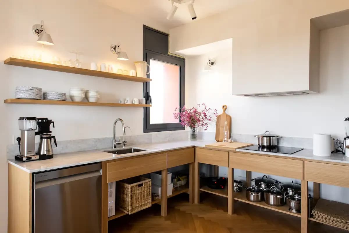 Fully equipped shared kitchen with wooden cabinetry, open shelving with dishes, a coffee machine, induction hob, and marble countertops.