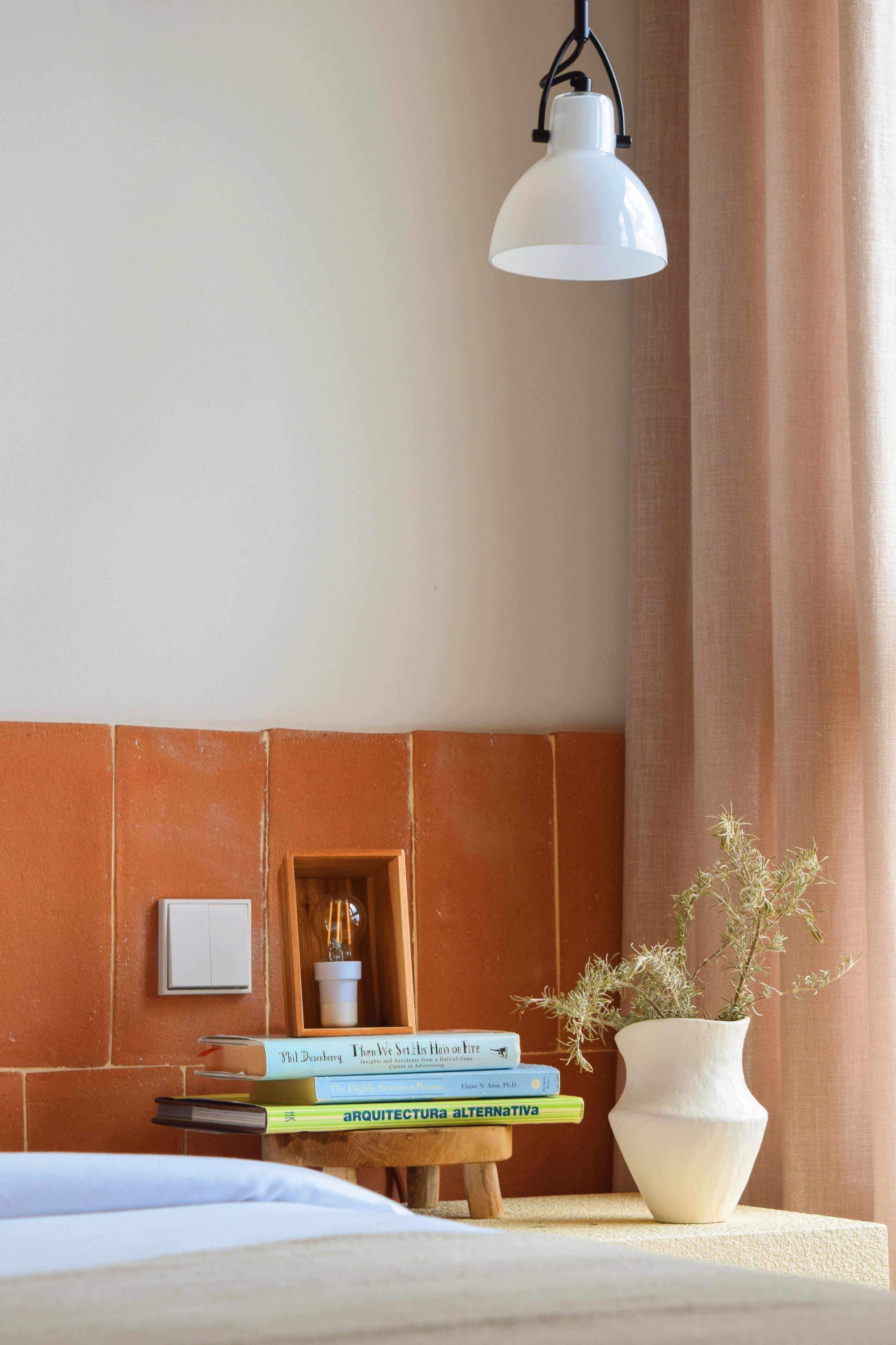 Close-up of a queen suite nightstand with a pendant lamp, books, a small vase, and terracotta tile headboard.