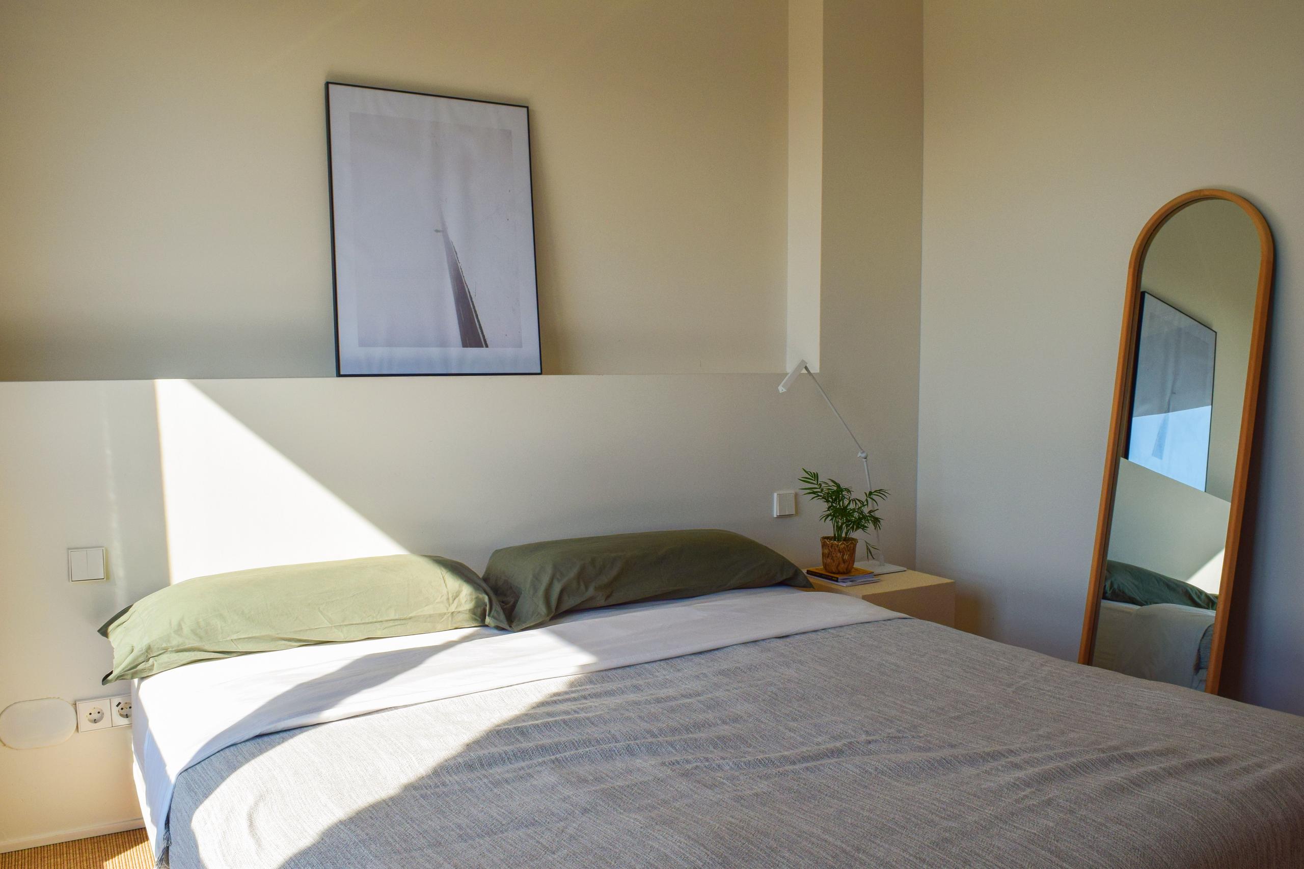 Bright king studio room with green bedding, a mirror, a plant, and natural light.