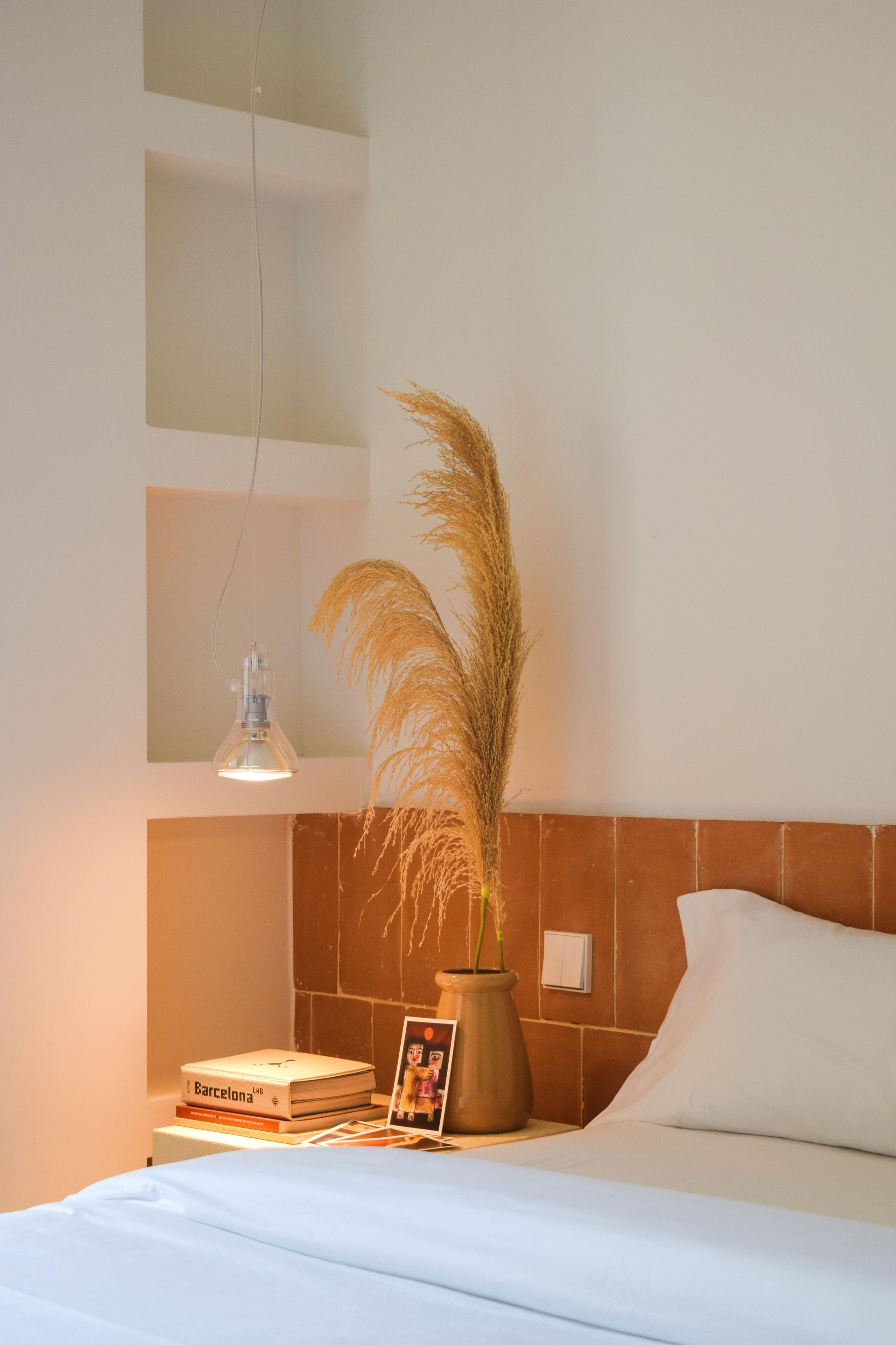 Queen room with a terracotta tile headboard, white bedding, a pendant lamp, and a vase with dried pampas grass.