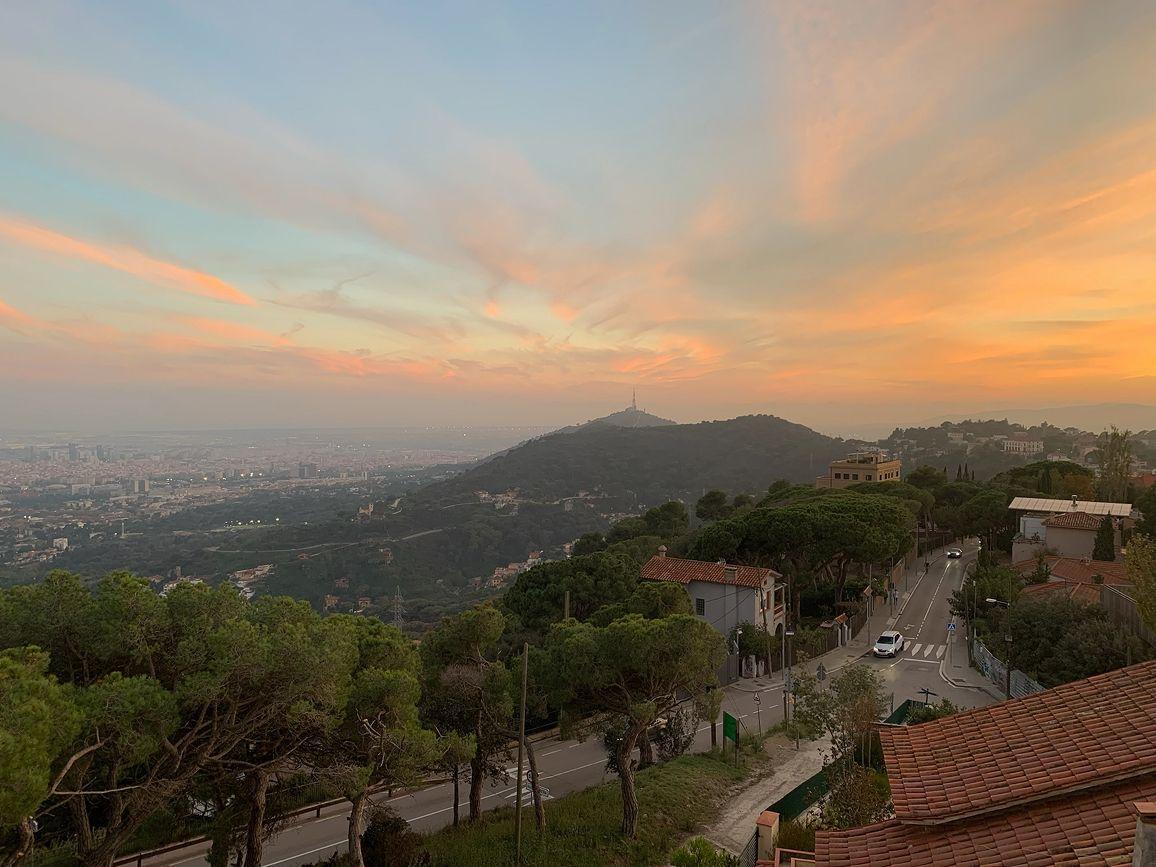 Panoramic sunset view of the Vallvidrera neighbourhood and Barcelona city from Circles House, with the Collserola tower and forest visible.