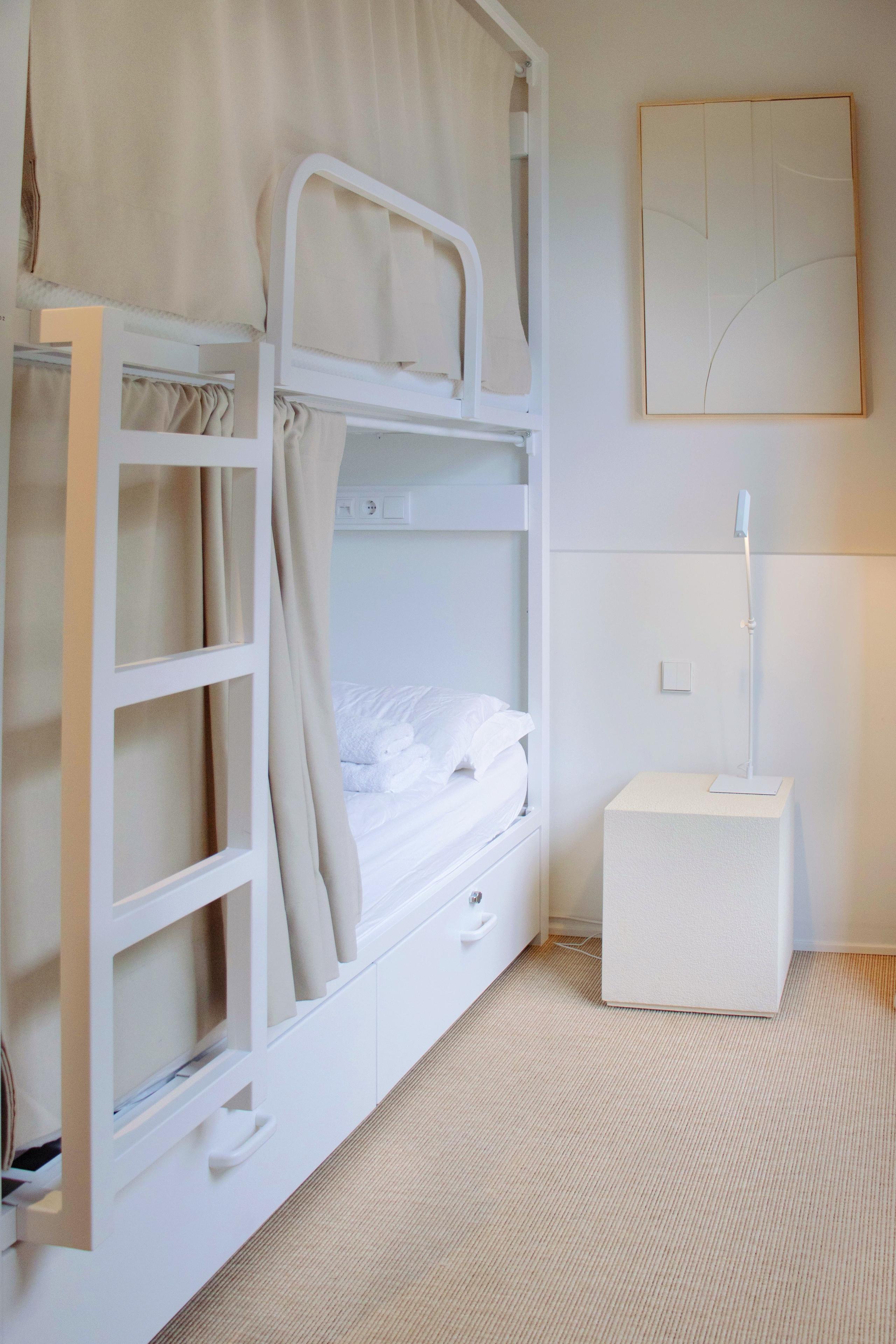 White bunk beds with privacy curtains and a bedside lamp in a shared suite.
