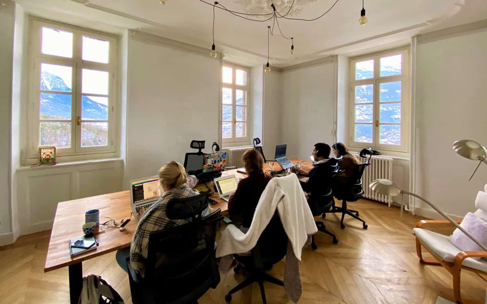 People working in a bright coworking room with mountain views through large windows