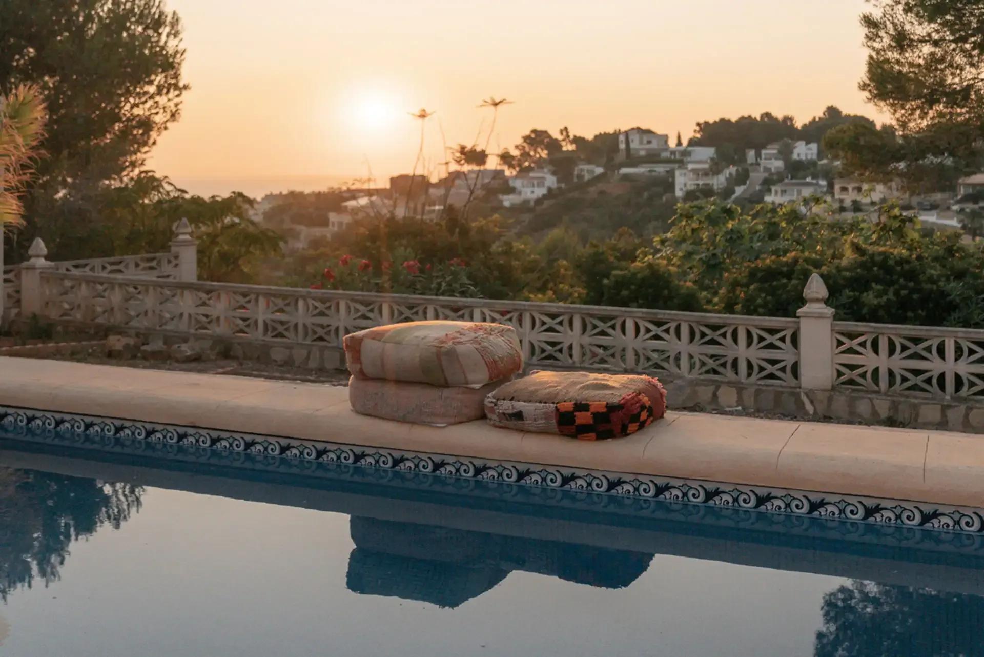 Pool area at sunset with cushions on the pool edge and a panoramic view of the surrounding hillside and sea