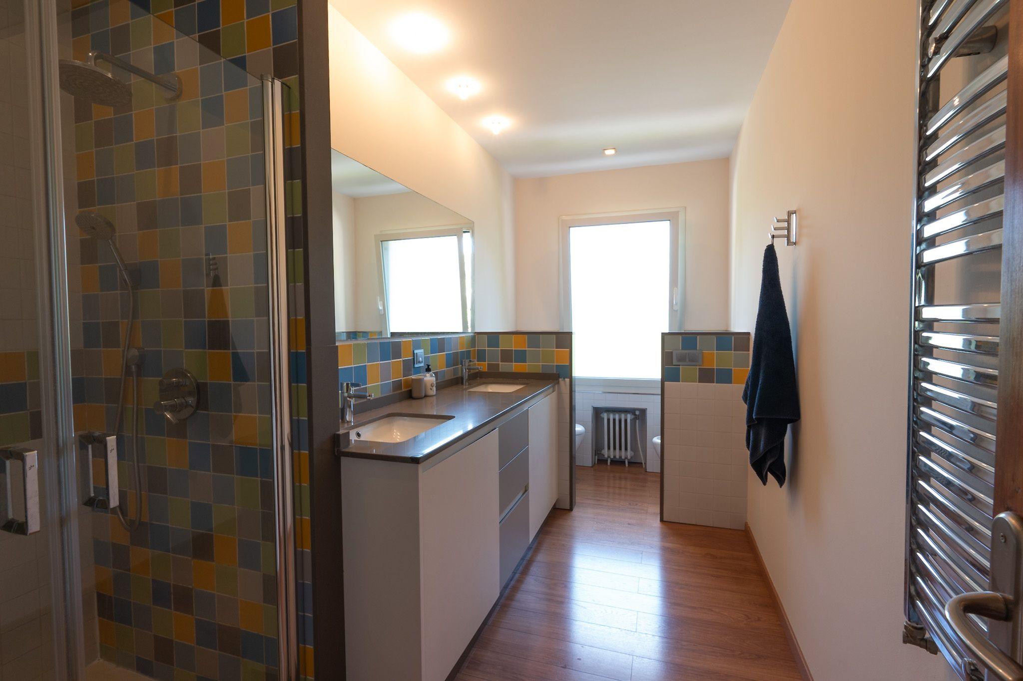 Shared bathroom with colorful tiled shower, double sink and mirror