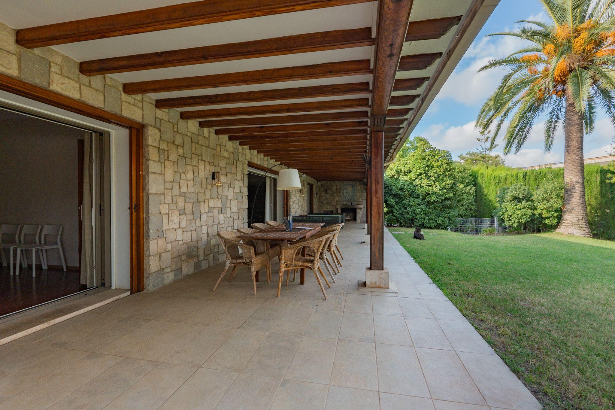 Stone-walled covered terrace with wooden beam ceiling, outdoor dining table, and garden view