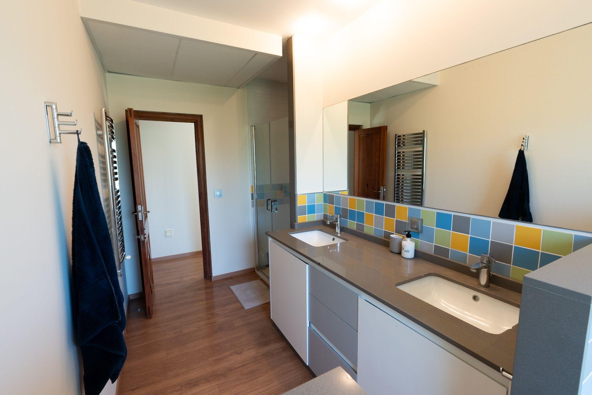 Shared bathroom with colorful tiled walls, double sink and shower