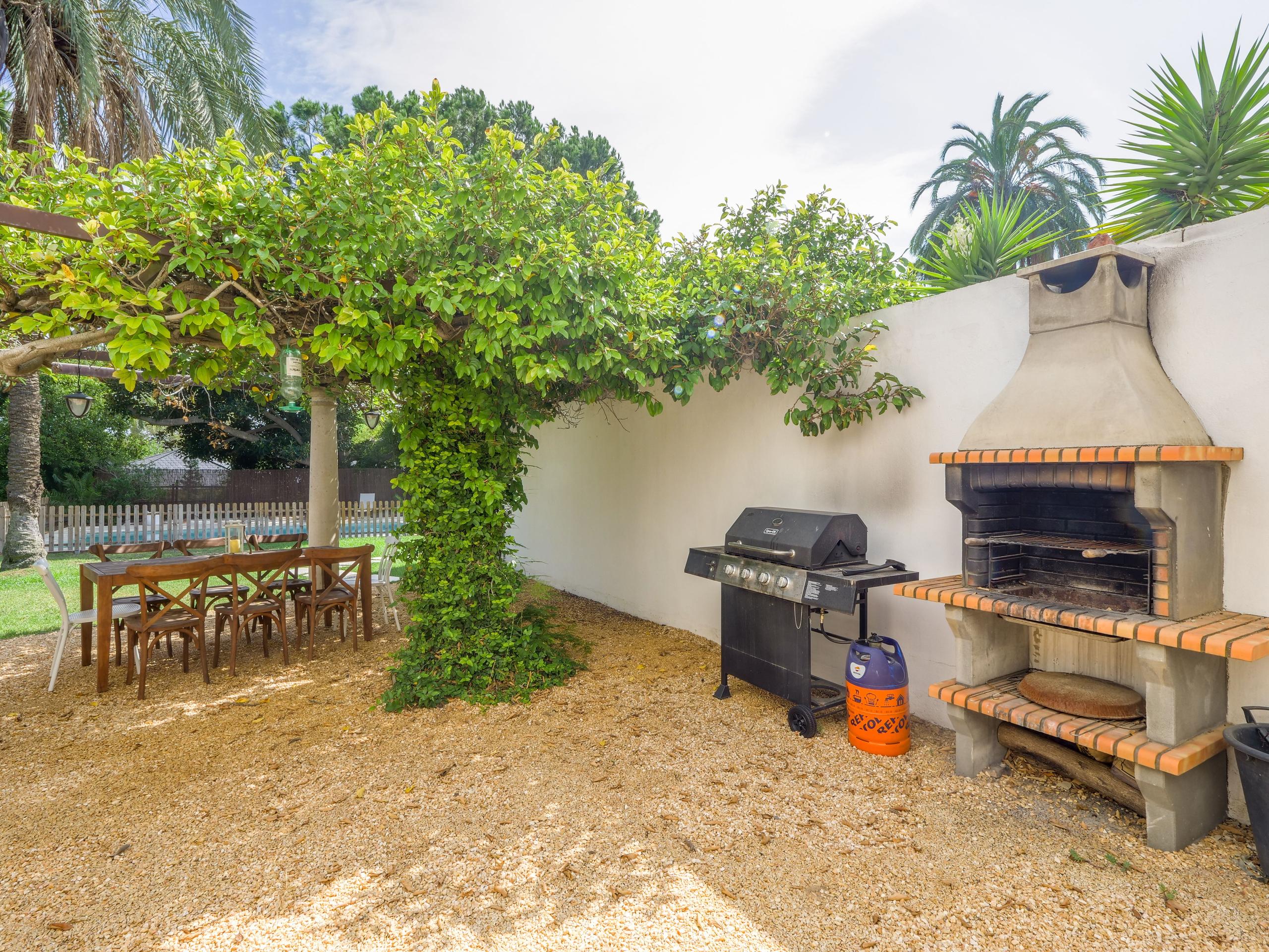 Outdoor BBQ area with gas grill, brick barbecue, and dining table under a tree