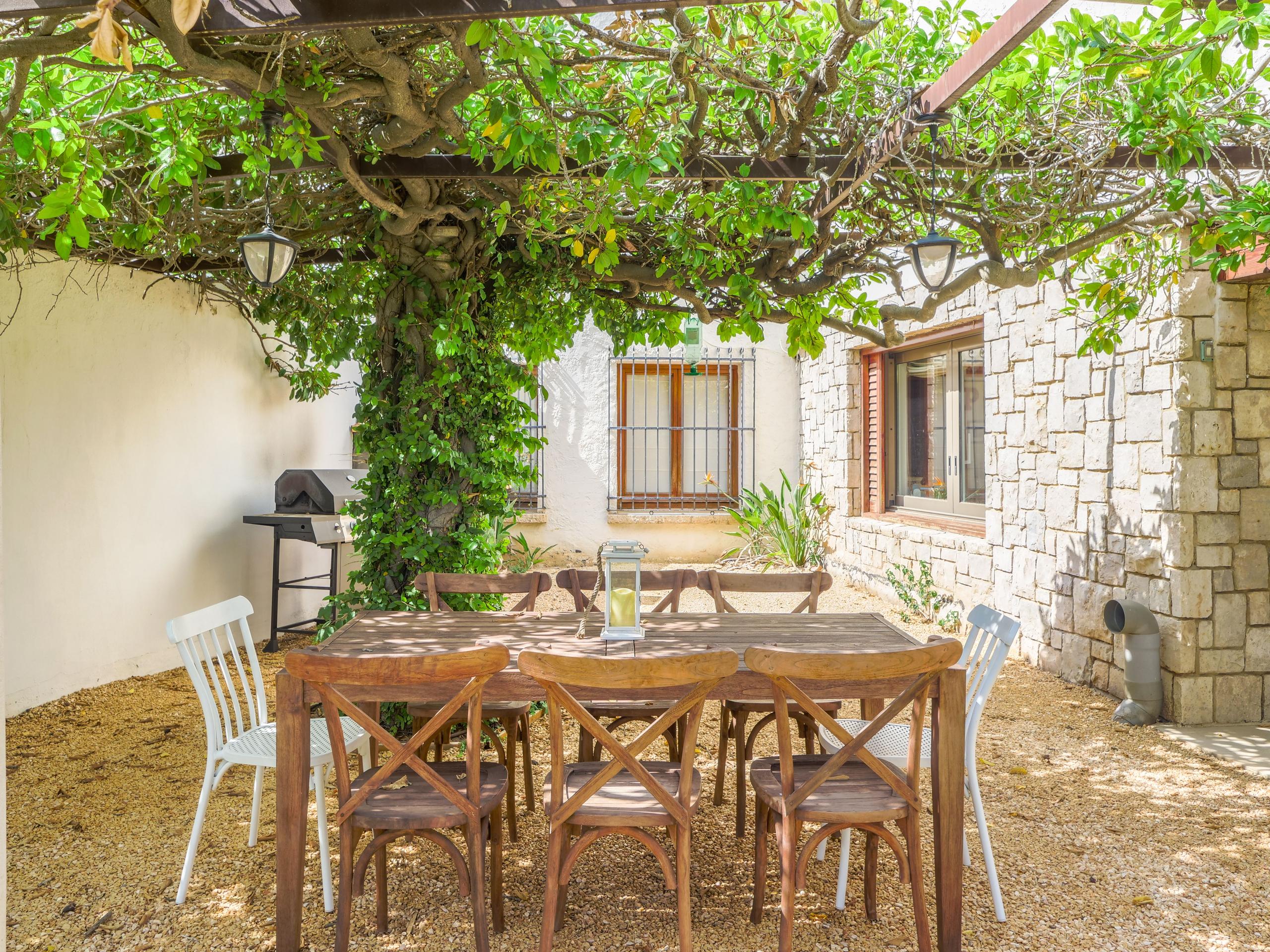 Outdoor dining table under a vine-covered pergola next to the villa's stone wall