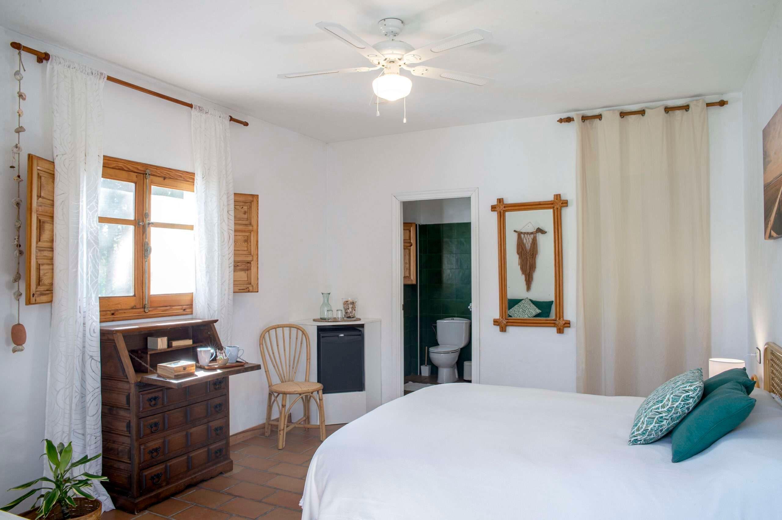 room with a big bed, a secretaire and a door open to the bathroom