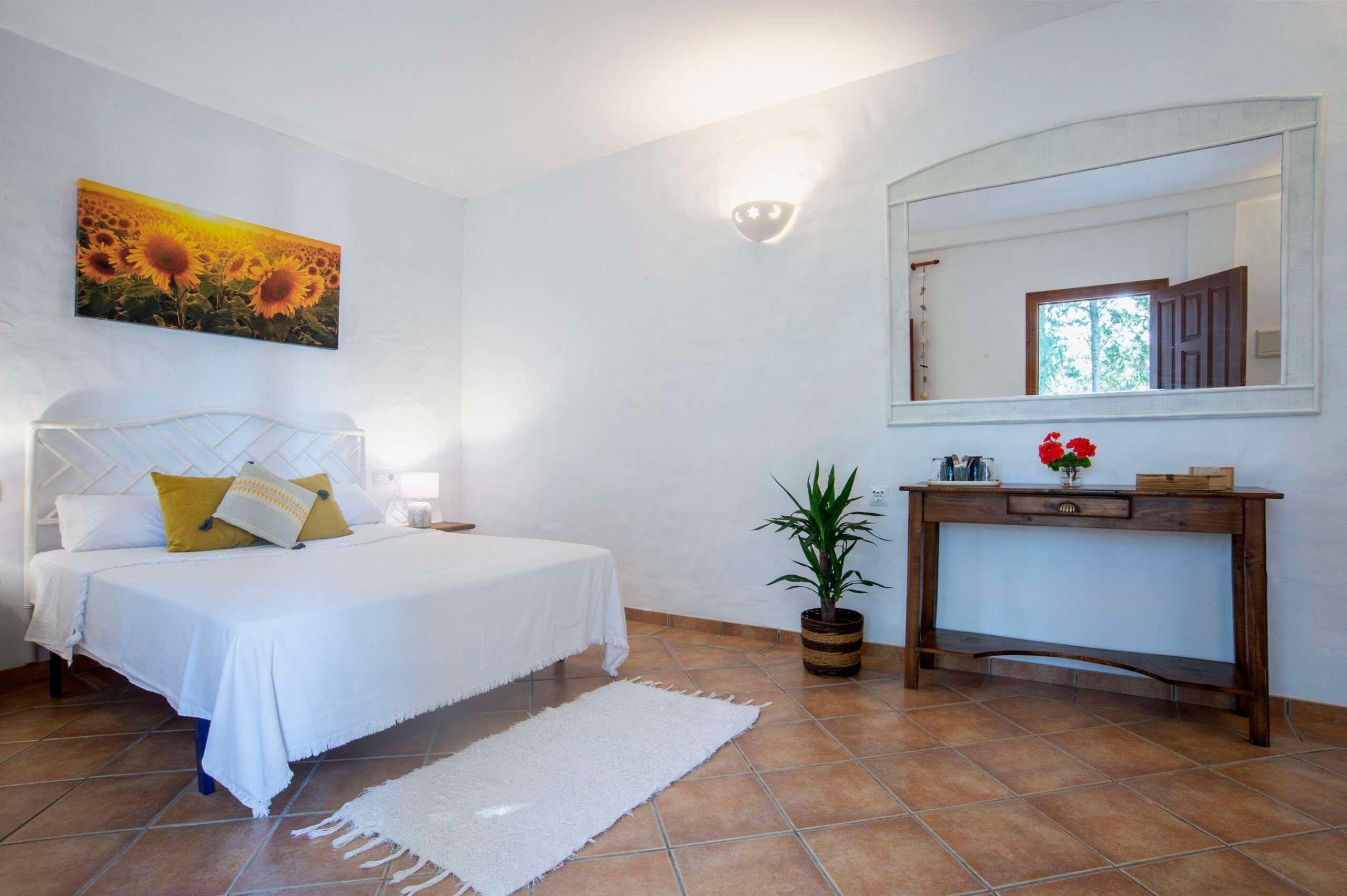 room with a double bed, a rug, a picture of sunflowers and a mirror