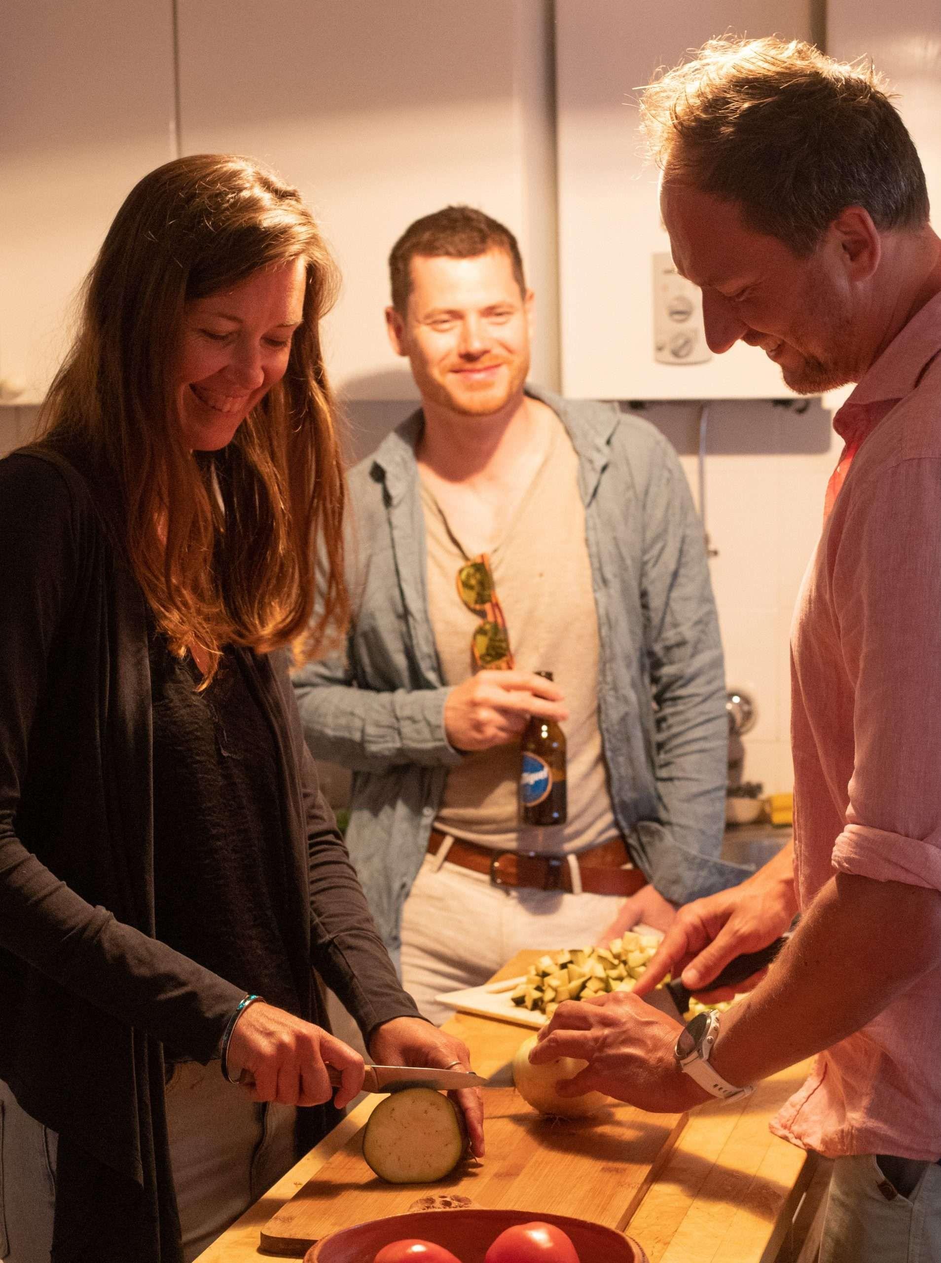3 people standing in a kitchen, cutting vegetables