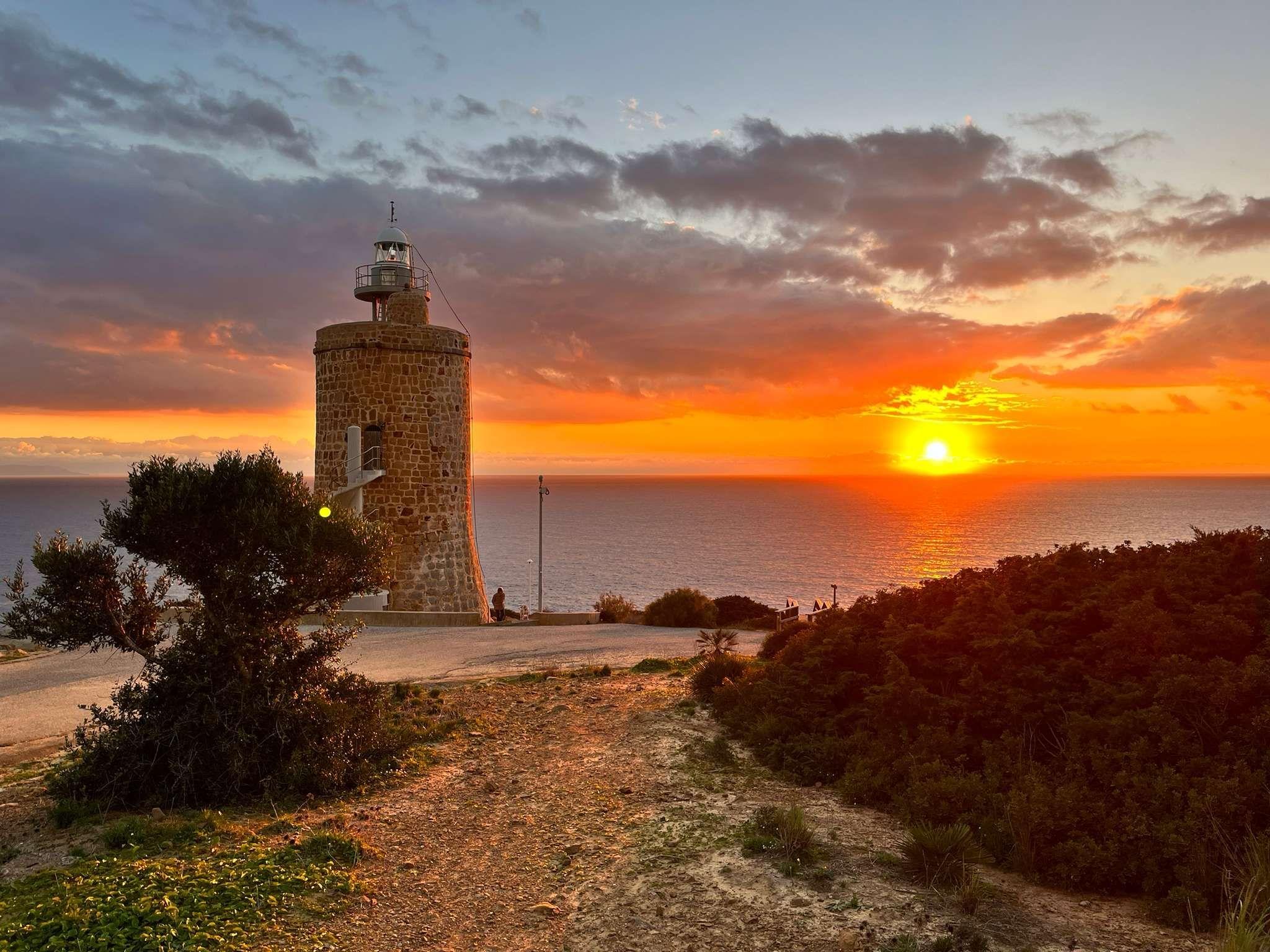 sun setting into the ocean, a lighthouse