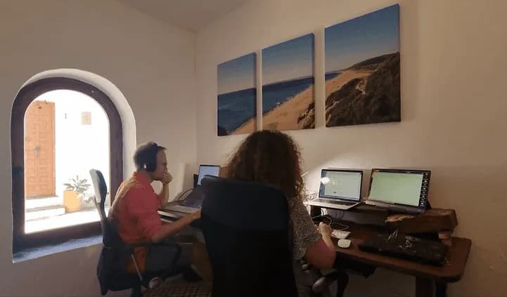 Two people working at desks in the dedicated office room with arched window and beach artwork on the wall