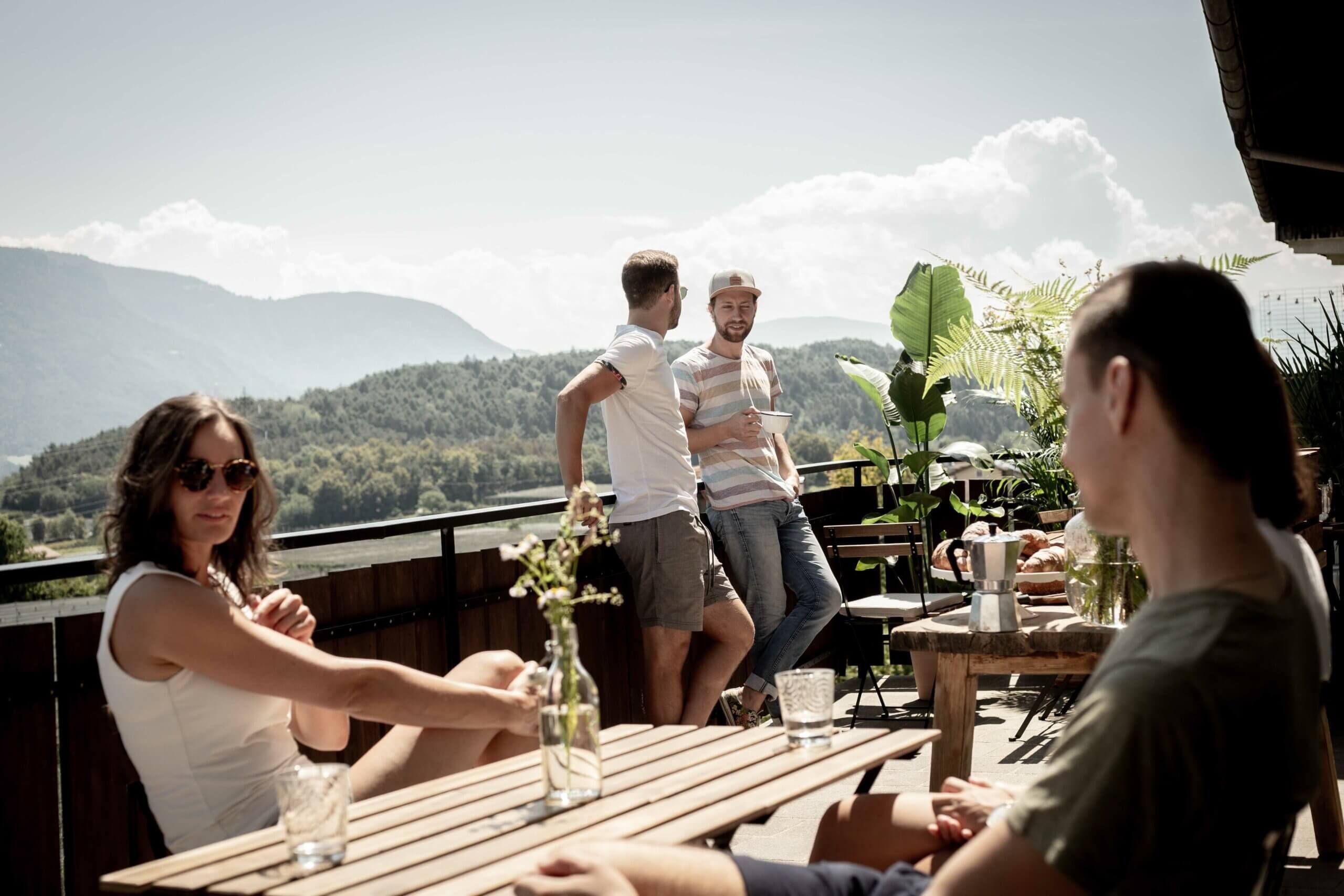 Group of guests socializing on the sunny terrace with mountain views in the background