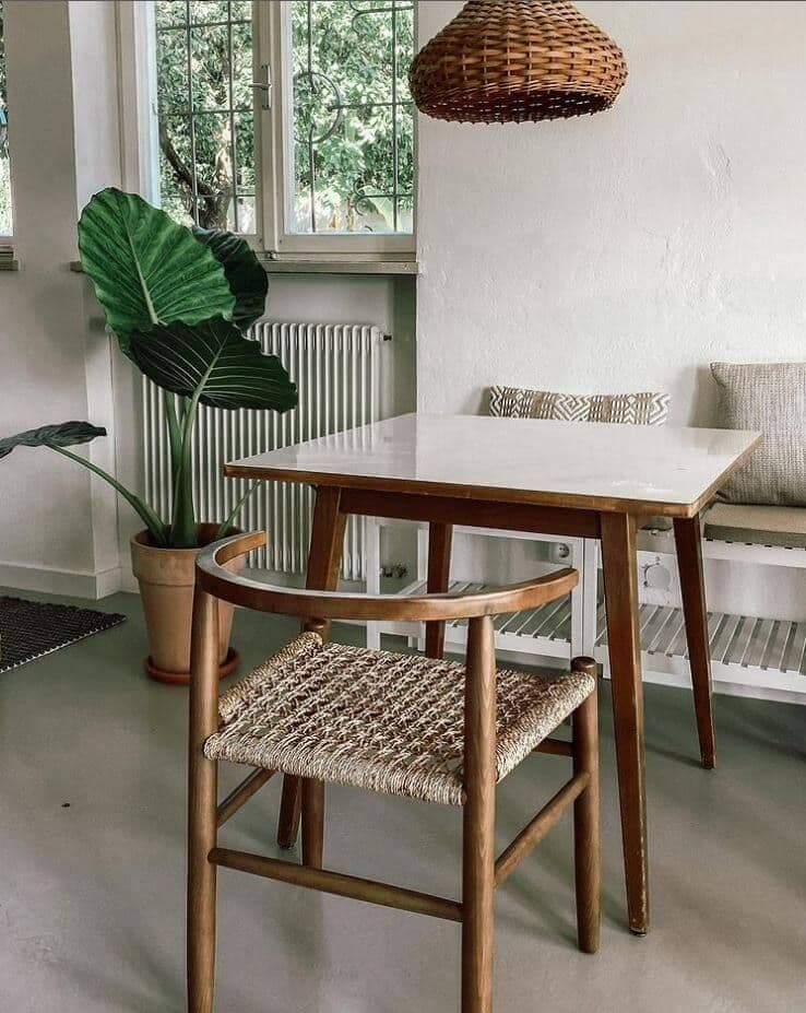 Cozy work cafe corner with a wooden table, woven chair, large tropical plant, and wicker pendant lamp