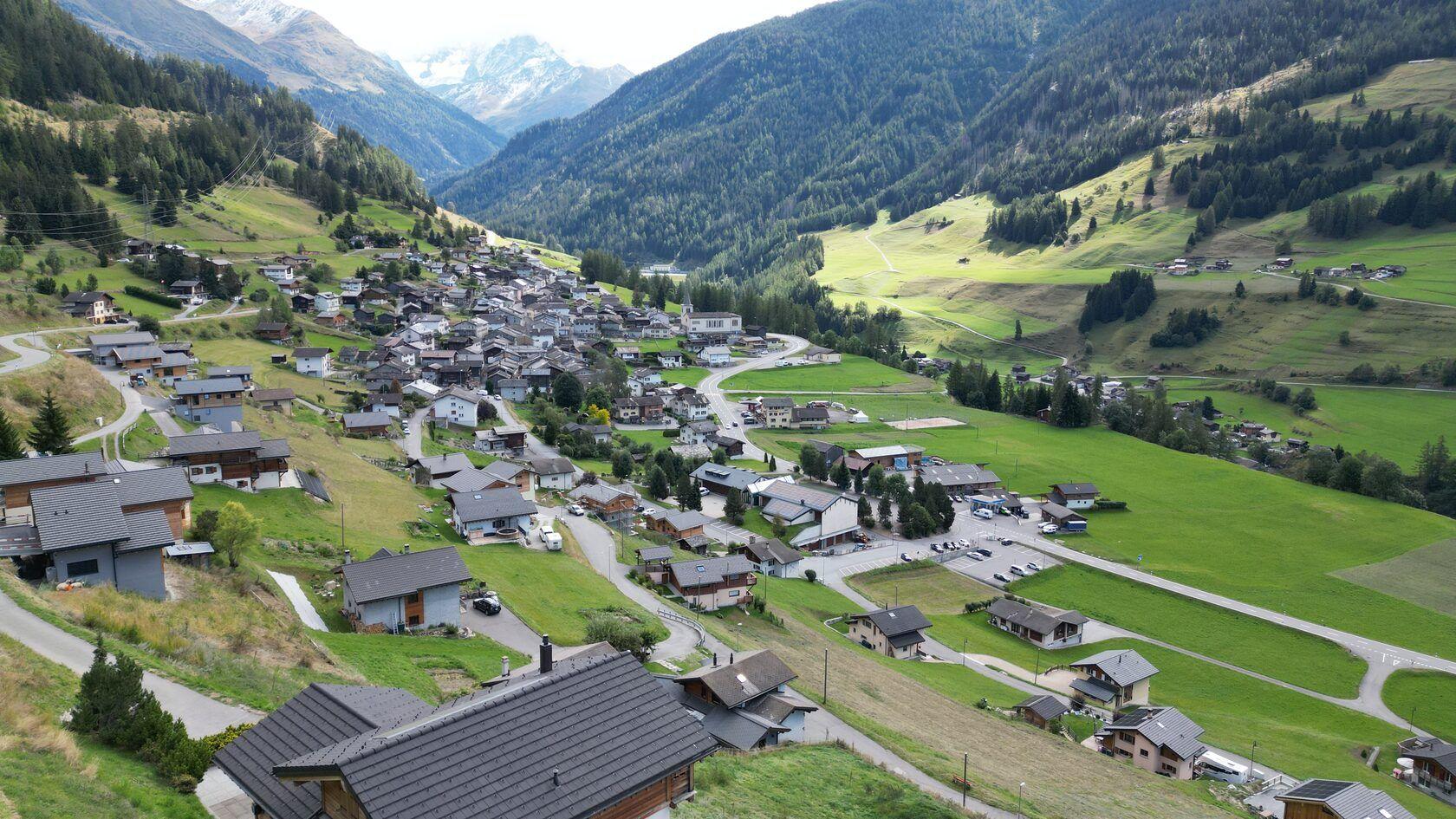 Drone aerial shot of Liddes village nestled in a green alpine valley with mountains and forests surrounding it