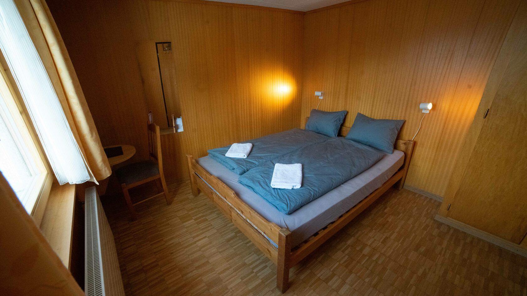 Private room with a double bed, wooden walls, warm ambient lighting, and a window