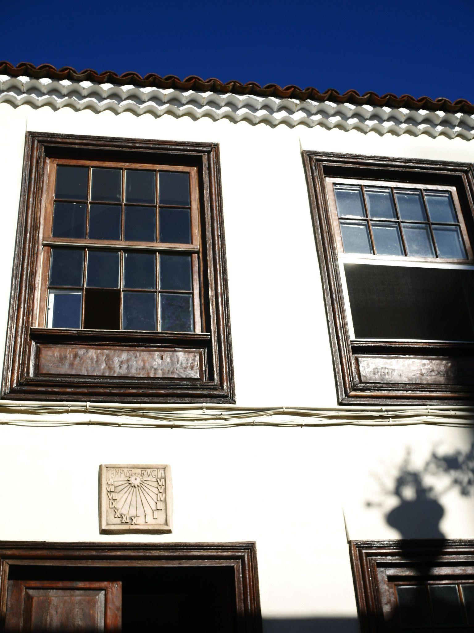 Close-up of the building exterior facade showing windows with dark wooden frames and a sundial plaque on the white wall