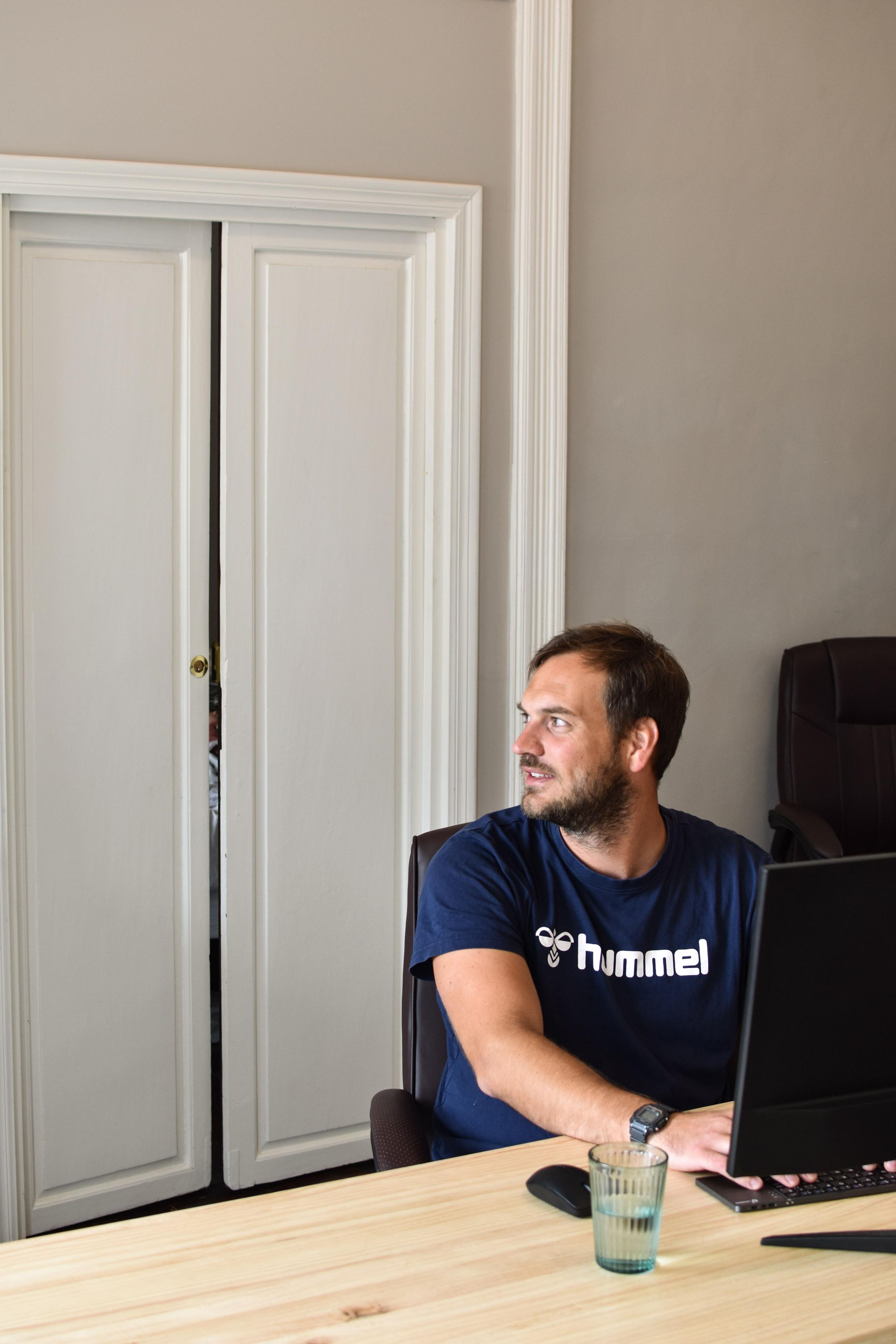 Man working on a laptop in a quiet room with a large wooden desk, likely the conference call room