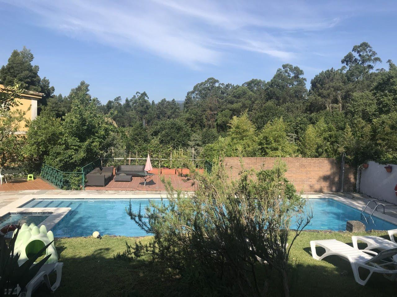 Outdoor swimming pool surrounded by garden and trees, with sun loungers and a terrace area